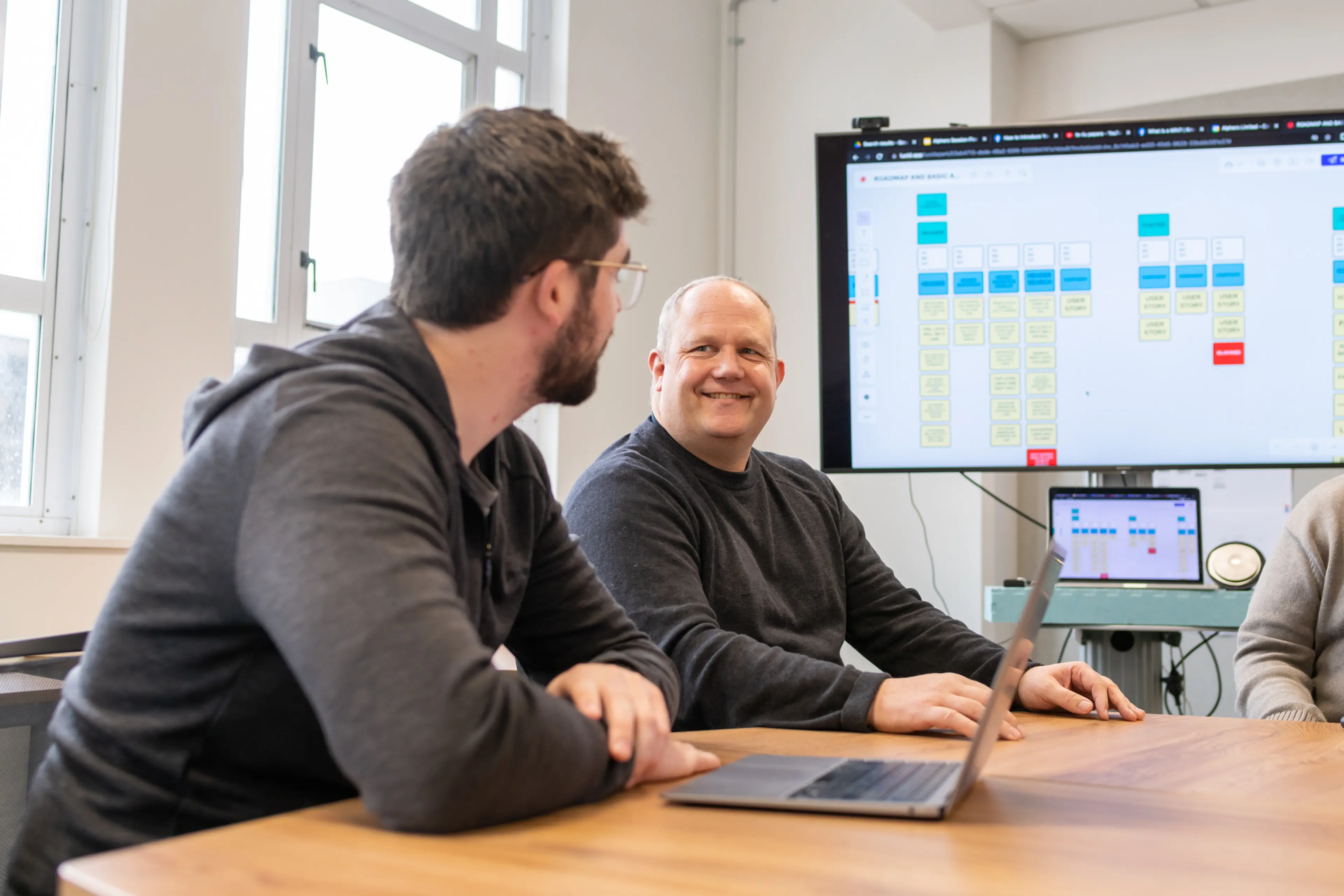 Two Alphero team members collaborating in a workshop, with a digital planning board displayed on screen in the background.