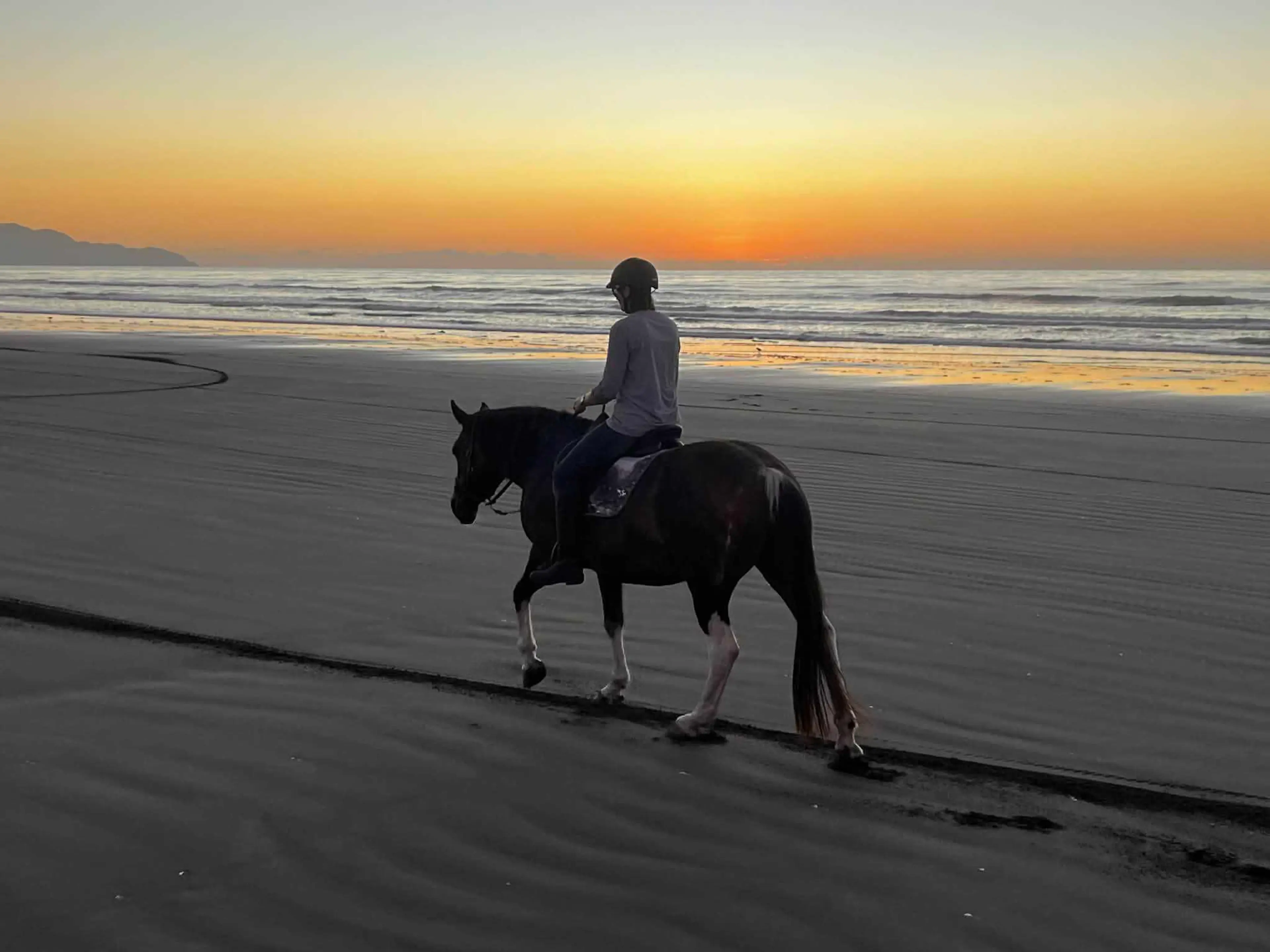 Person on horseback, walking along a beach at sunset