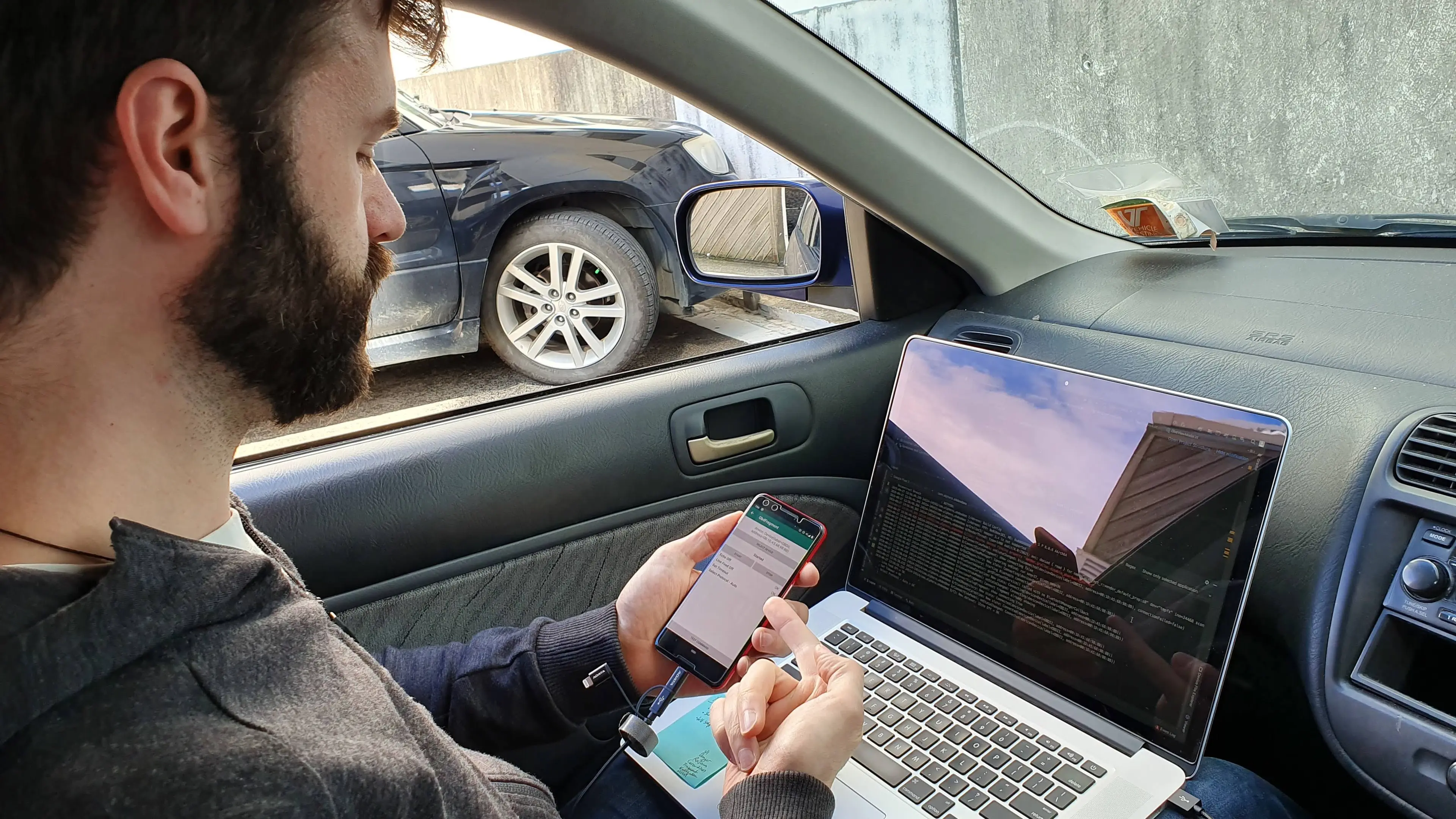 Man in a car with a laptop and mobile phone in his lap