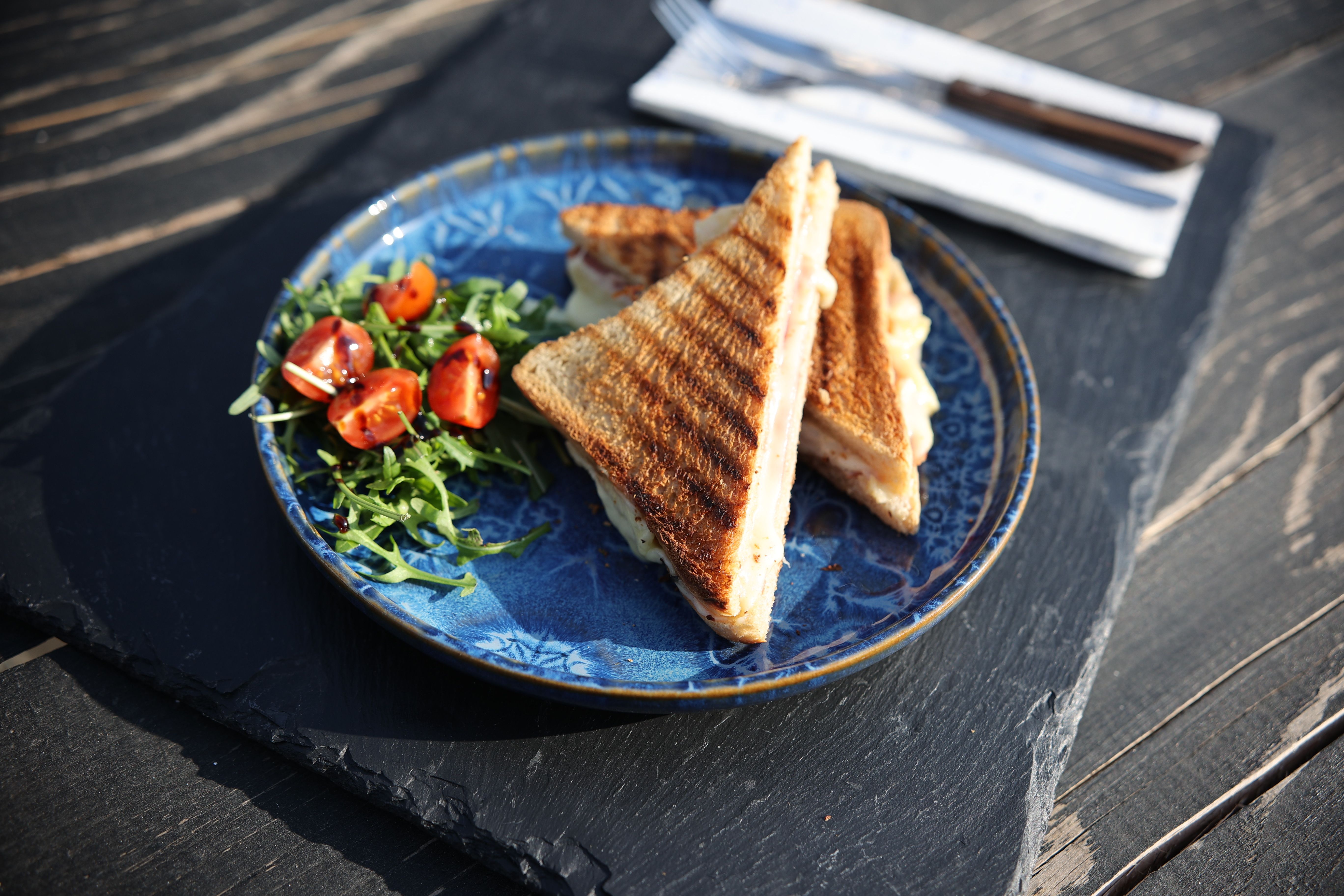 Porto Toast – Gegrilltes Sandwich mit Schinken und Käse, serviert mit Rucola und Tomaten im Gastgarten der Porto Bar Gratwein