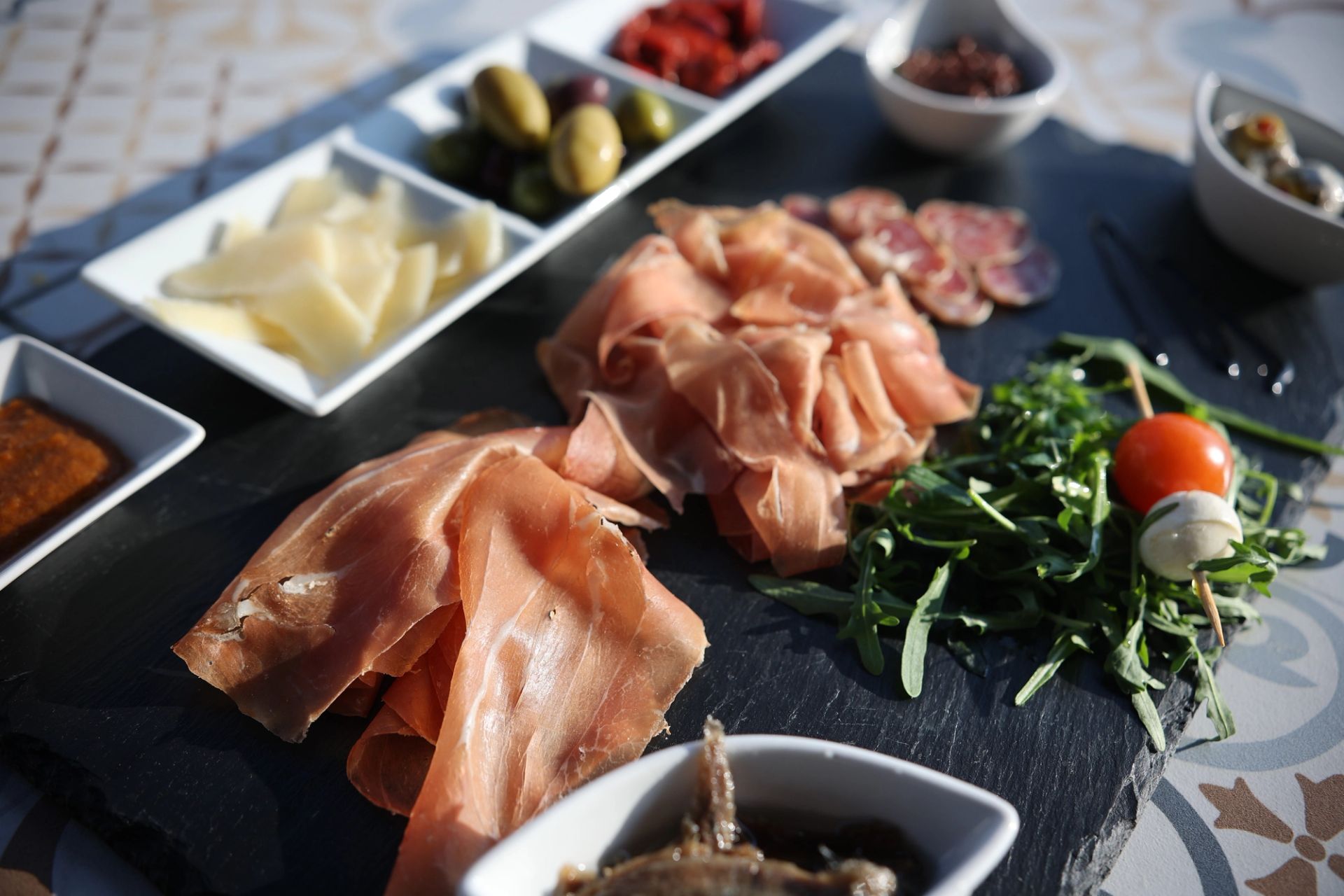Mediterraner Mix – Antipasti-Platte mit Prosciutto, Oliven, Käse und getrockneten Tomaten auf Schieferplatte in der Porto Bar Gratwein
