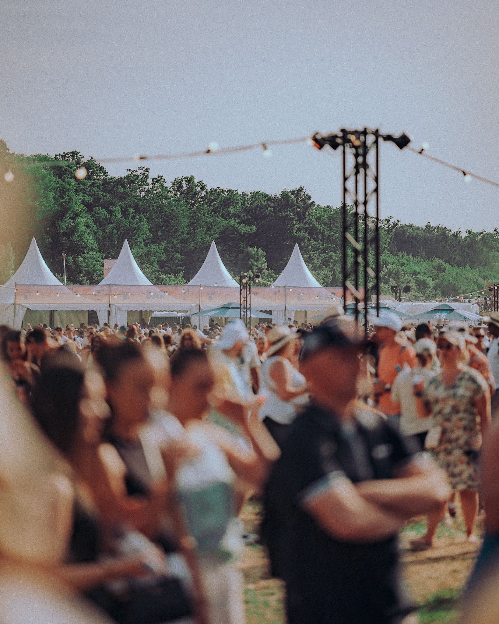 Foule sur le site du festival, avec des tentes blanches et des guirlandes lumineuses en arrière-plan