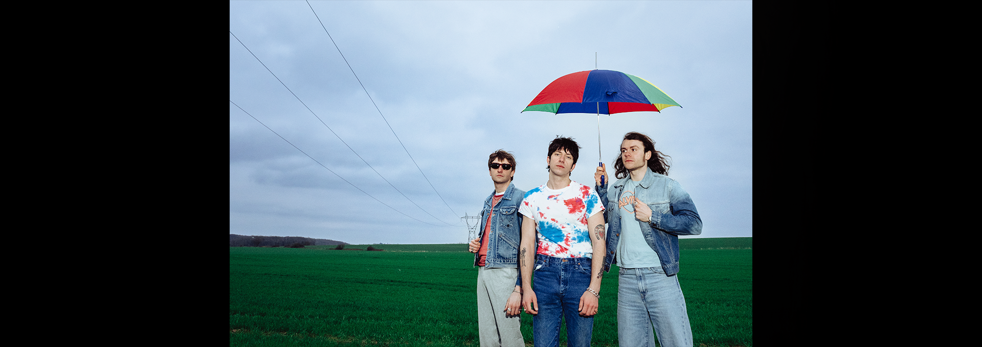 Howlin' Jaws, trois musiciens en vestes en jean sous un parapluie multicolore dans un champ