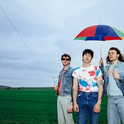 Howlin' Jaws, trois musiciens en vestes en jean sous un parapluie multicolore dans un champ