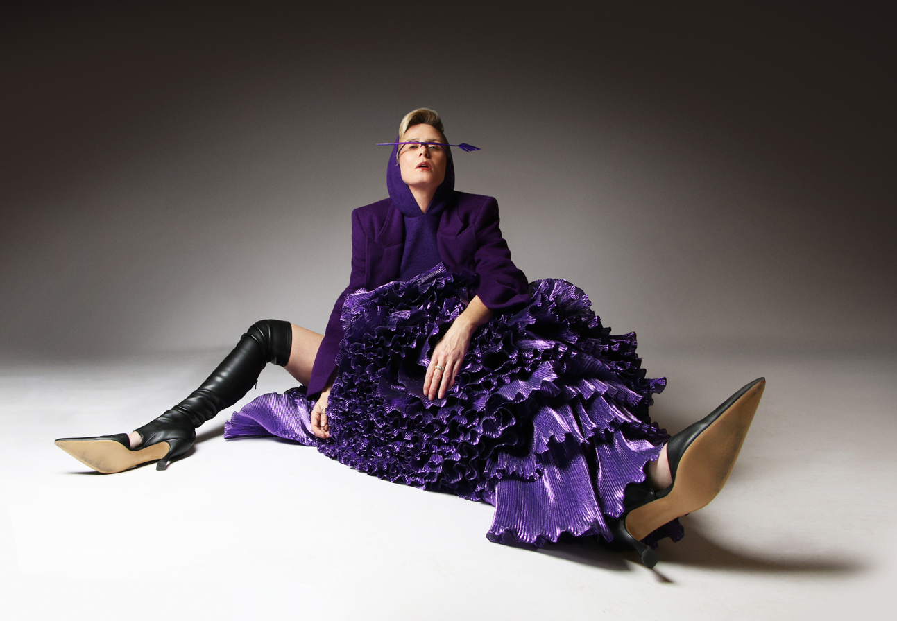 Róisín Murphy allongée dans une tenue violette plissée et des bottes noires, sur fond gris