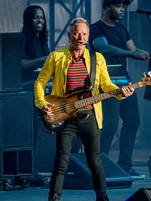 Sting en veste jaune jouant de la basse sur scène, entouré de ses musiciens