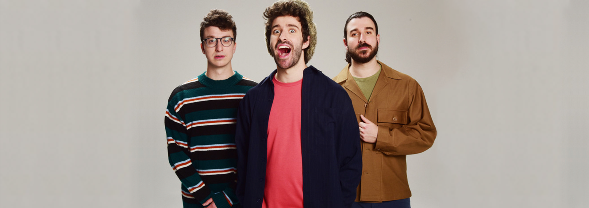Portrait de groupe des trois membres d'AJR, posant sur un fond clair uni