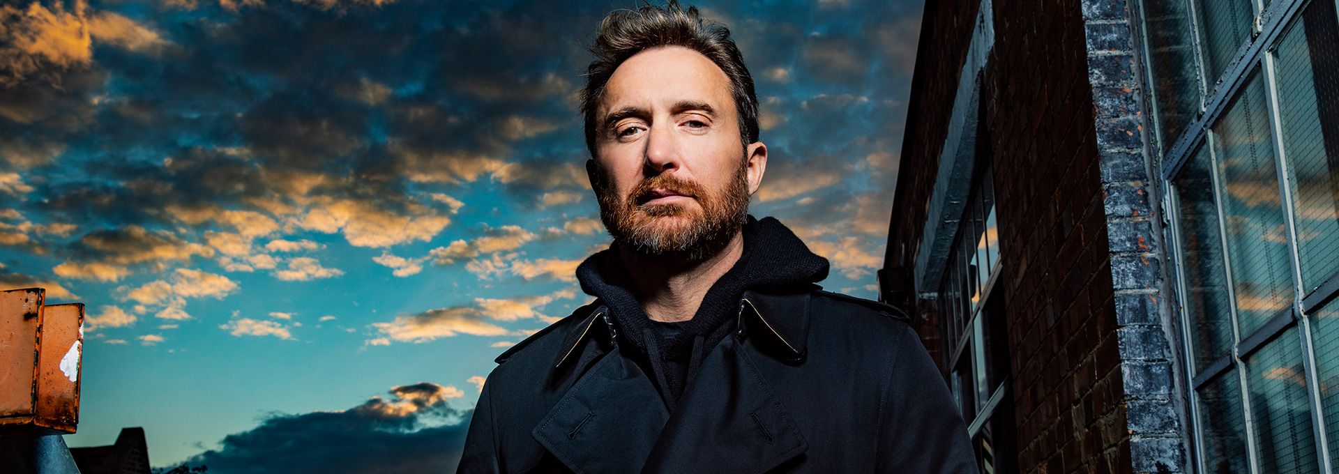 Portrait de David Guetta en manteau sombre, ciel nuageux en arrière-plan