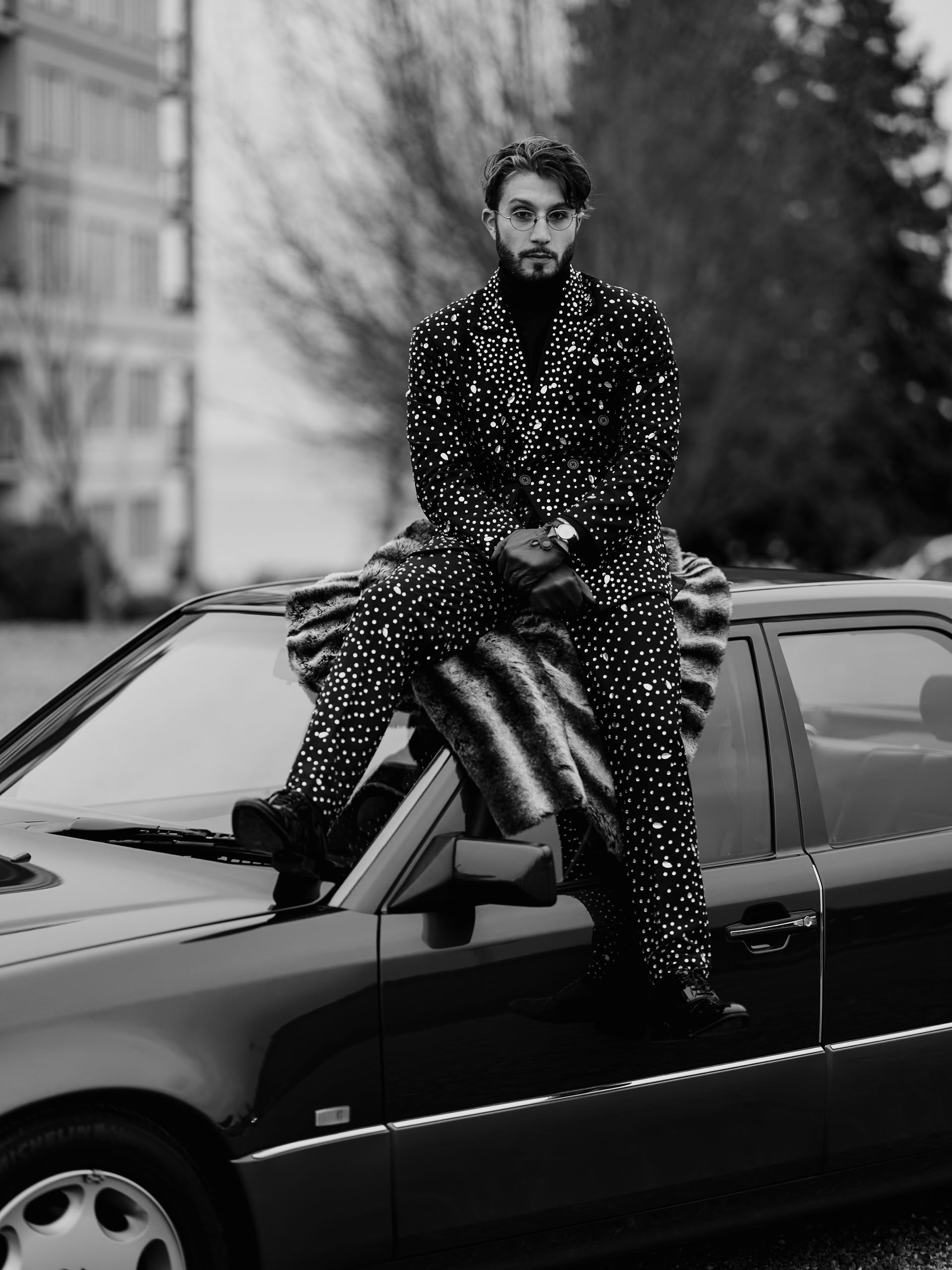 Portrait en noir et blanc de bbno$, assis sur le capot d'une voiture en costume à strass