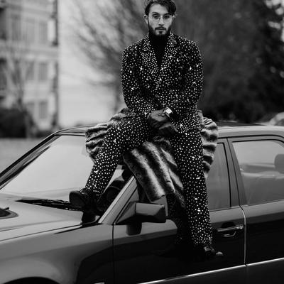 Portrait en noir et blanc de bbno$, assis sur le capot d'une voiture en costume à strass
