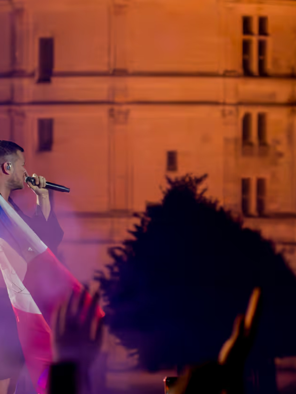 Chanteur d'Imagine Dragons brandissant un drapeau français sur scène, façade du château de Chambord derrière lui
