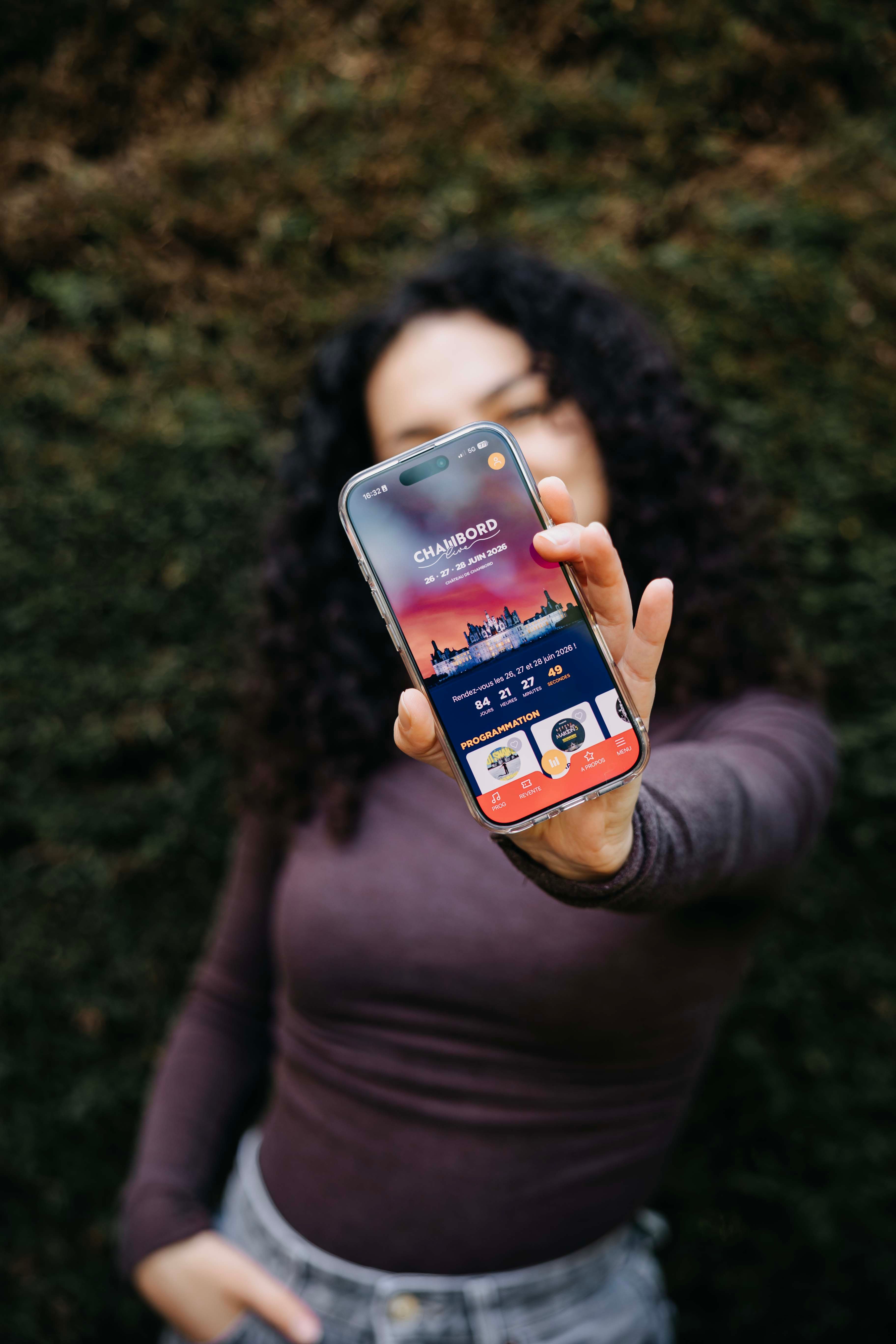 Main tendant un smartphone affichant l'application Chambord Live, les 26, 27 et 28 juin 2026