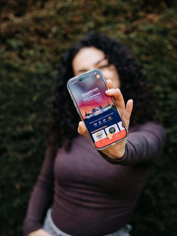 Main tendant un smartphone affichant l'application Chambord Live, les 26, 27 et 28 juin 2026