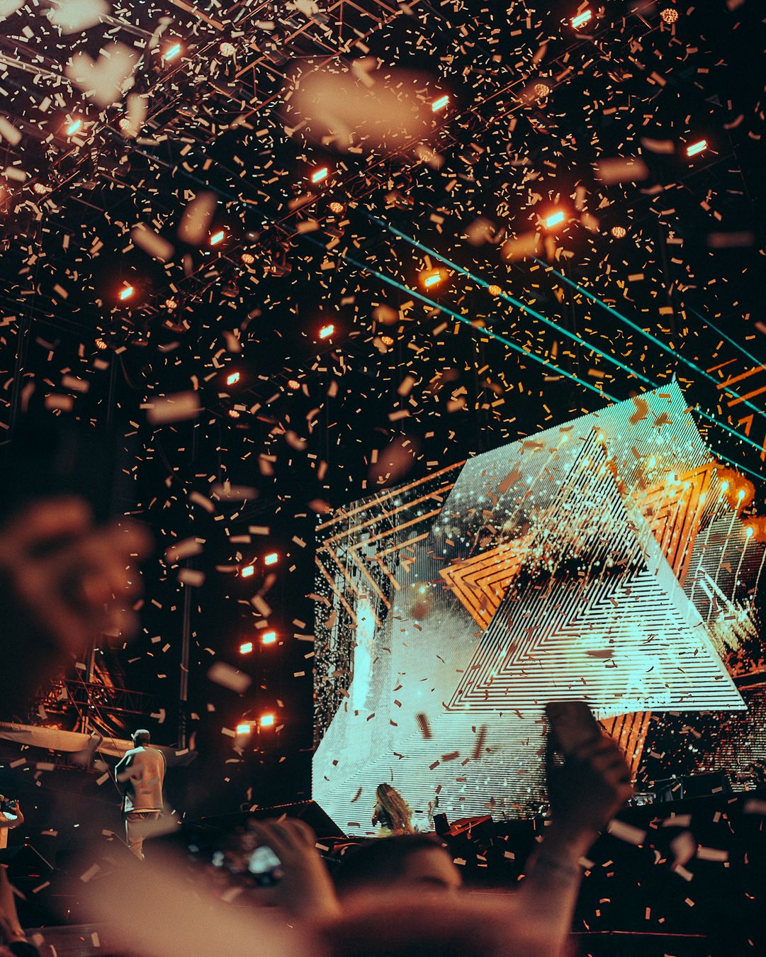 Pluie de confettis dorés devant un grand écran lumineux de la scène, mains levées dans le public