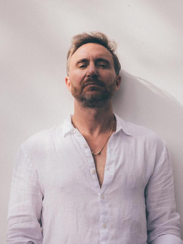 Portrait de David Guetta en chemise blanche, adossé à un mur clair