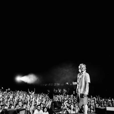 Orelsan debout sur scène face au public, photo en noir et blanc