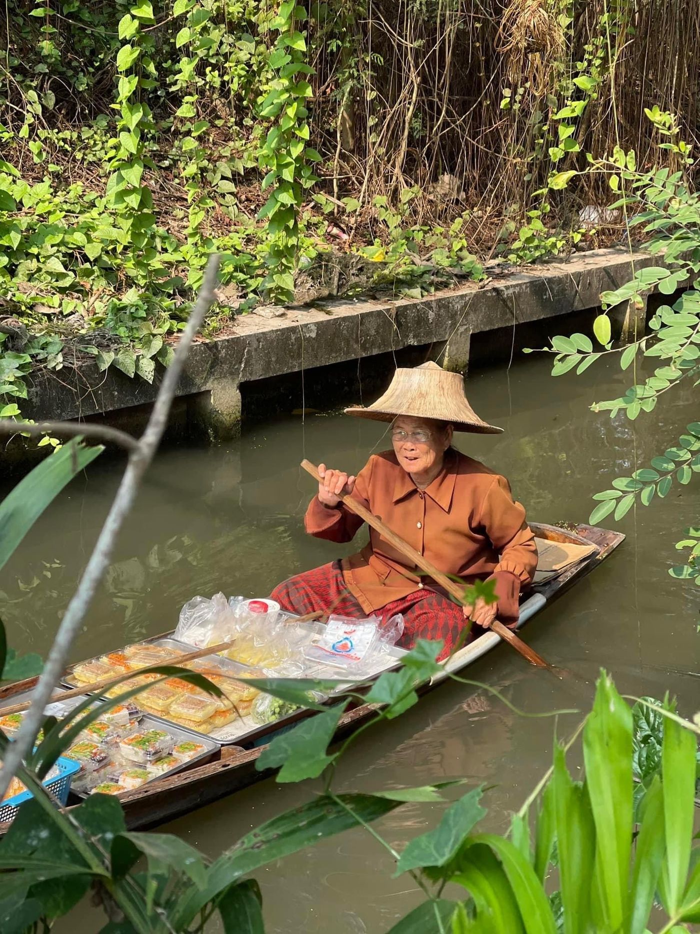 Una vendedora en su embarcación, a lo largo de un canal tailandés.