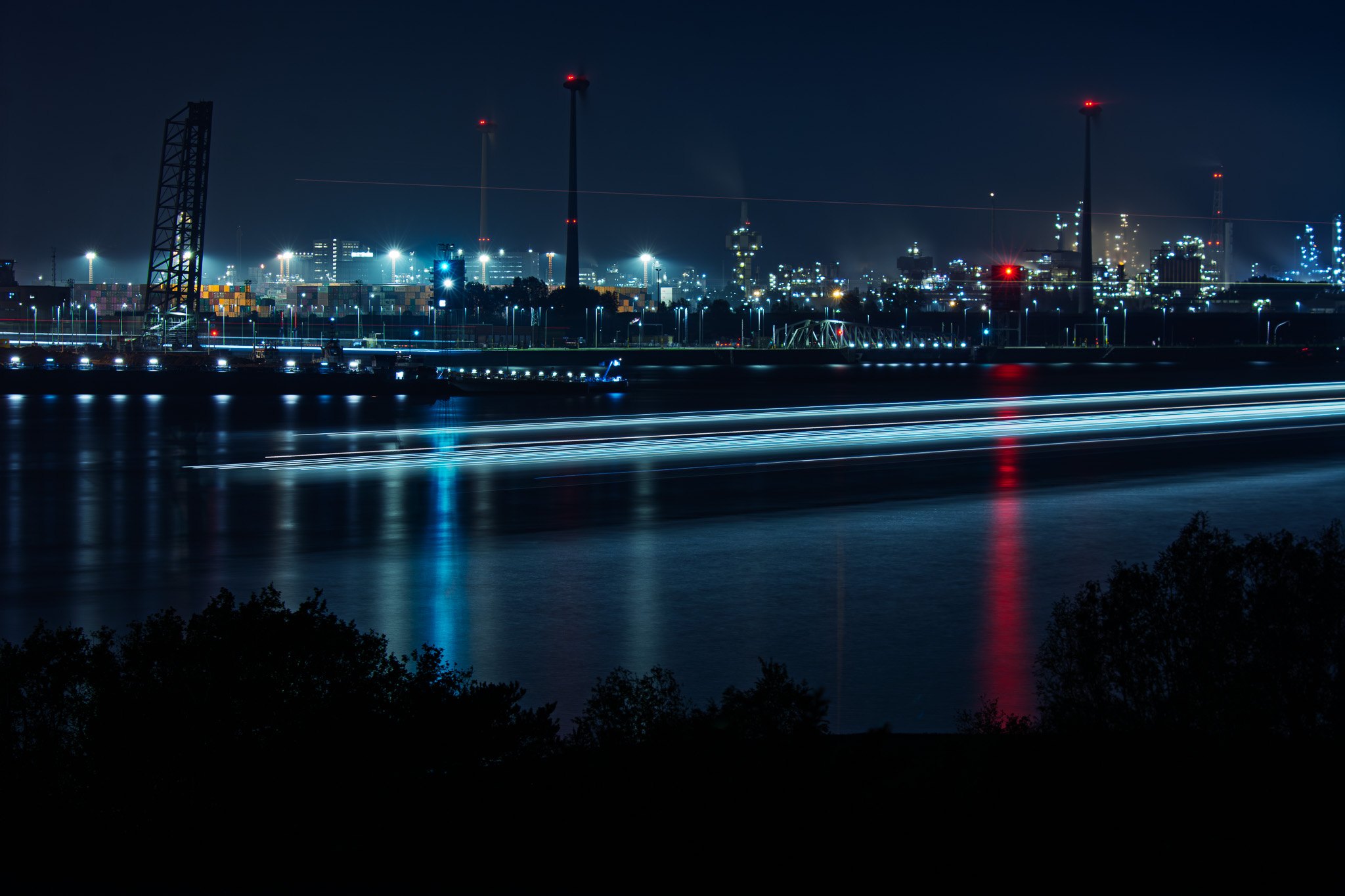 In front of an industrial harbour scenery in the night a boat appears as a long lightline
