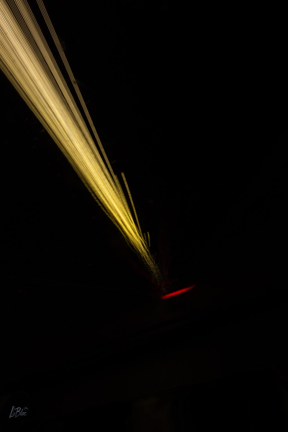 Dense golden light trails converge through deep black beside a small red signal