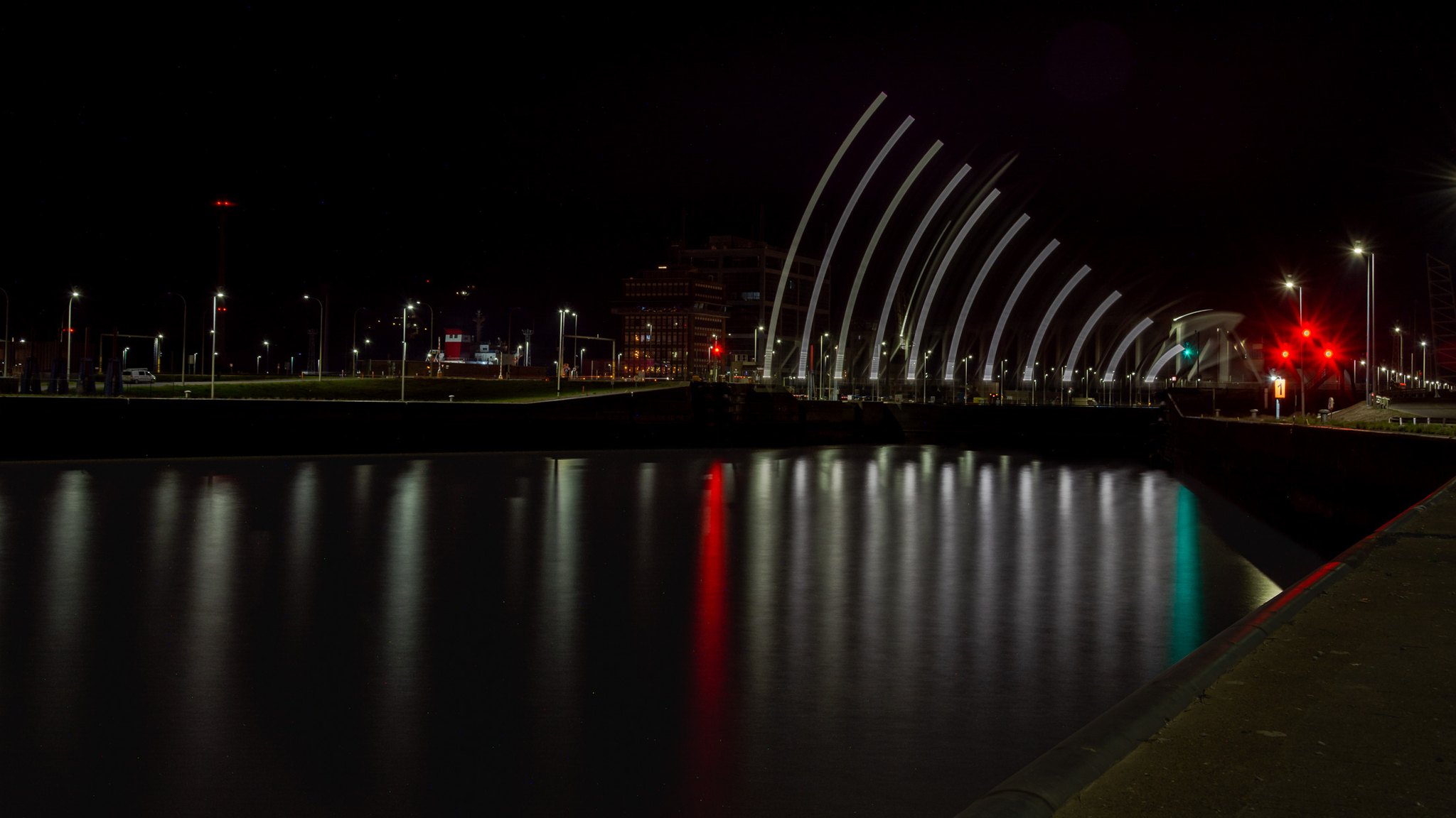 A lock slowly closes at night. Its movement appears as a fan of pale, rib-like traces above the dark water. These repeated forms record the closing movement rather than a row of separate, fixed arches.