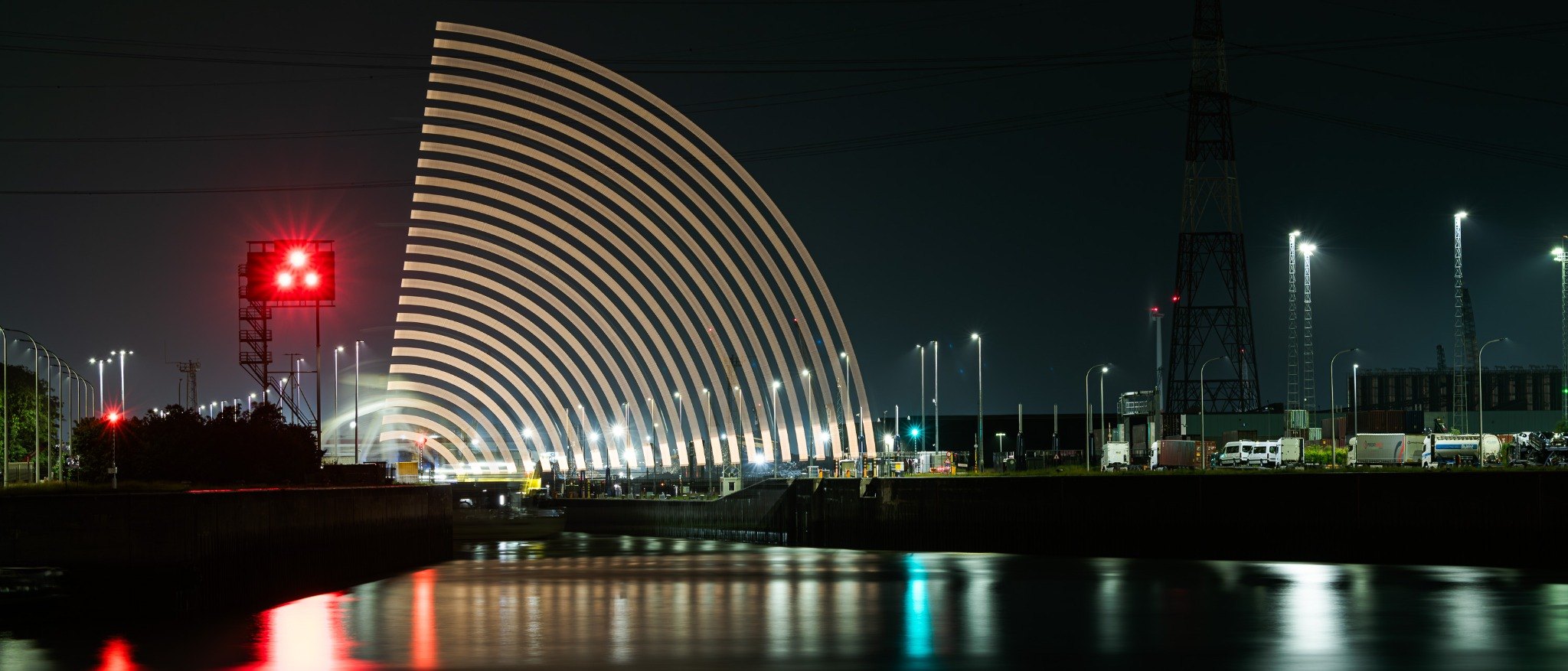 A white arc of repeated light rises beside red signals at the Kallo lock