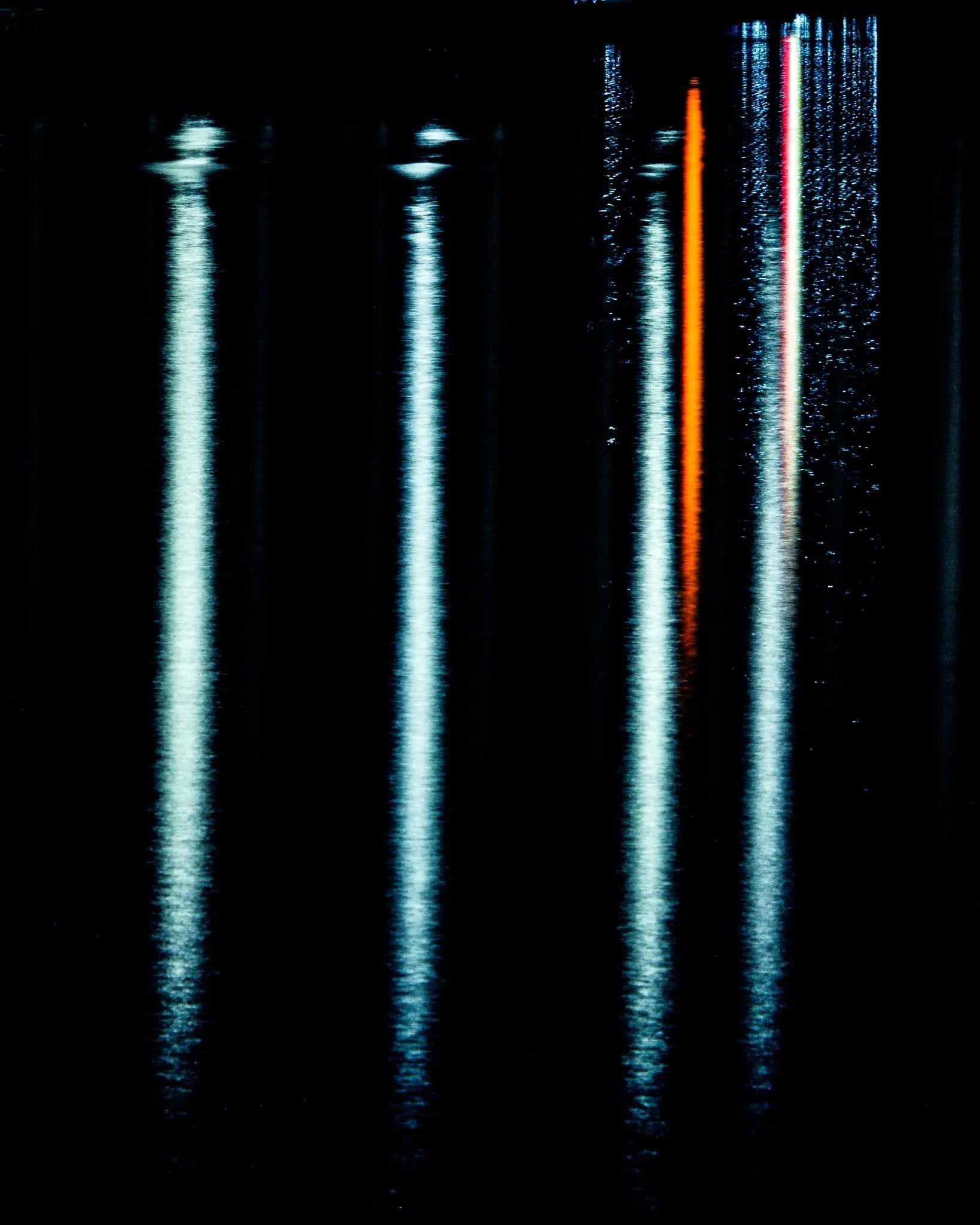 Vertical cyan-white and orange reflections suspended in black water