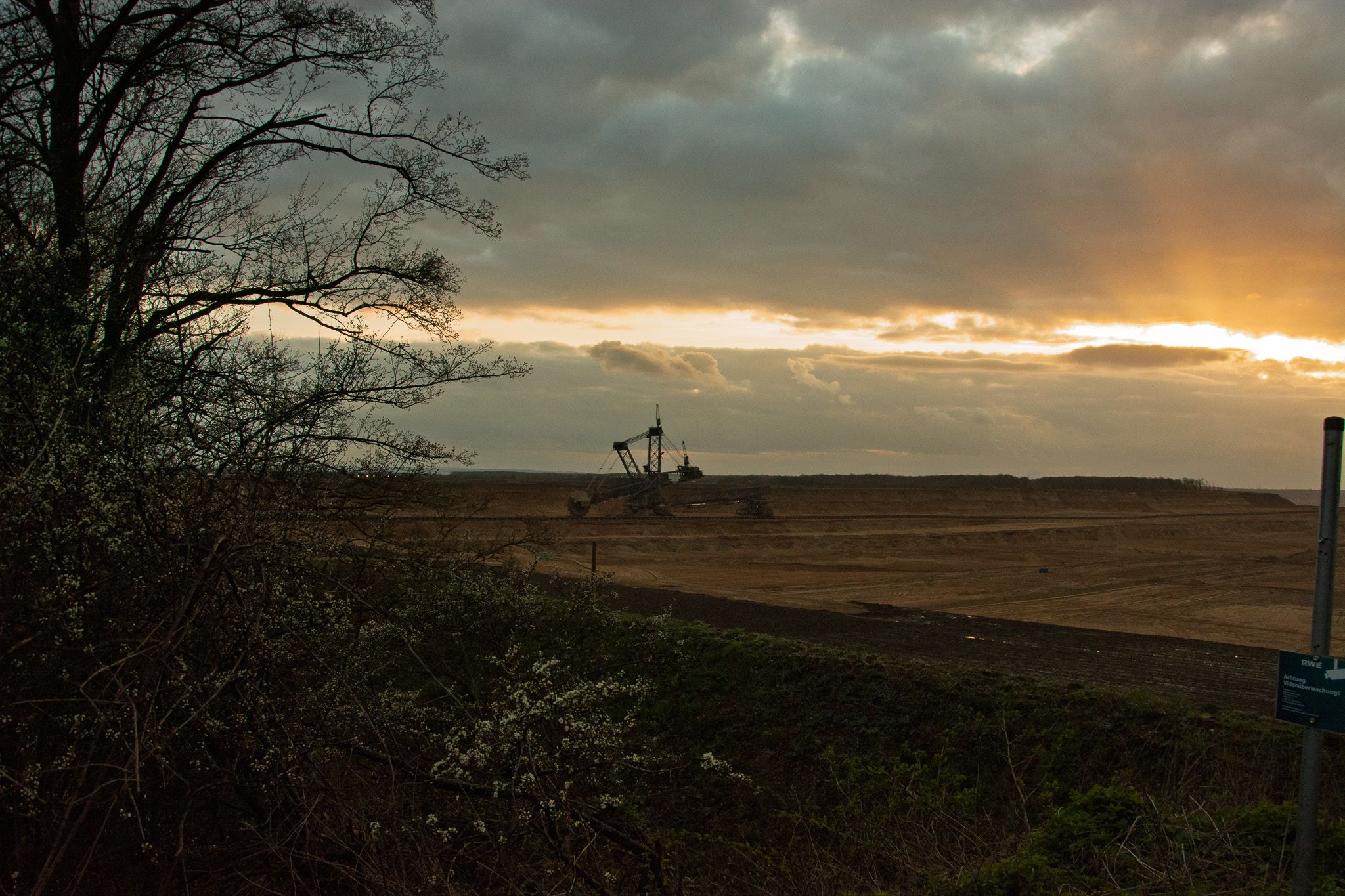 An open mine and distant excavator beneath a heavy break in the clouds