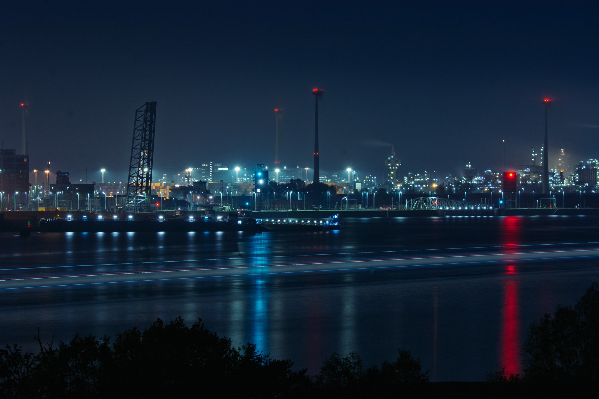 In front of an industrial harbour scenery in the night a boat appears as a long lightline
