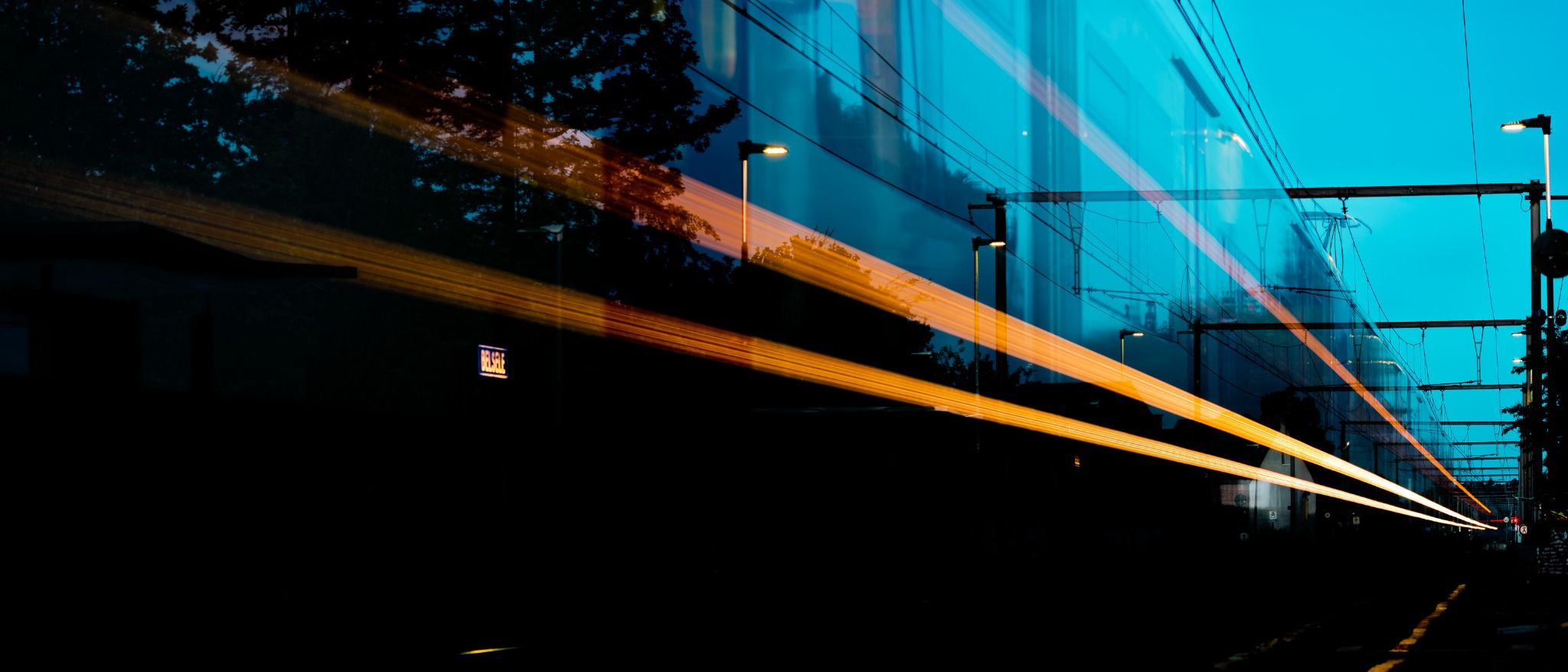 Amber train light crossing a blue railway corridor at dusk
