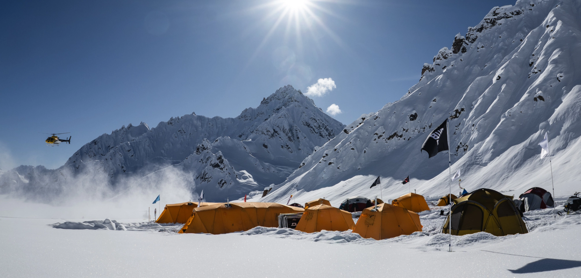 A ski base camp with a lot of tents and a helicopter hovering in the distance.