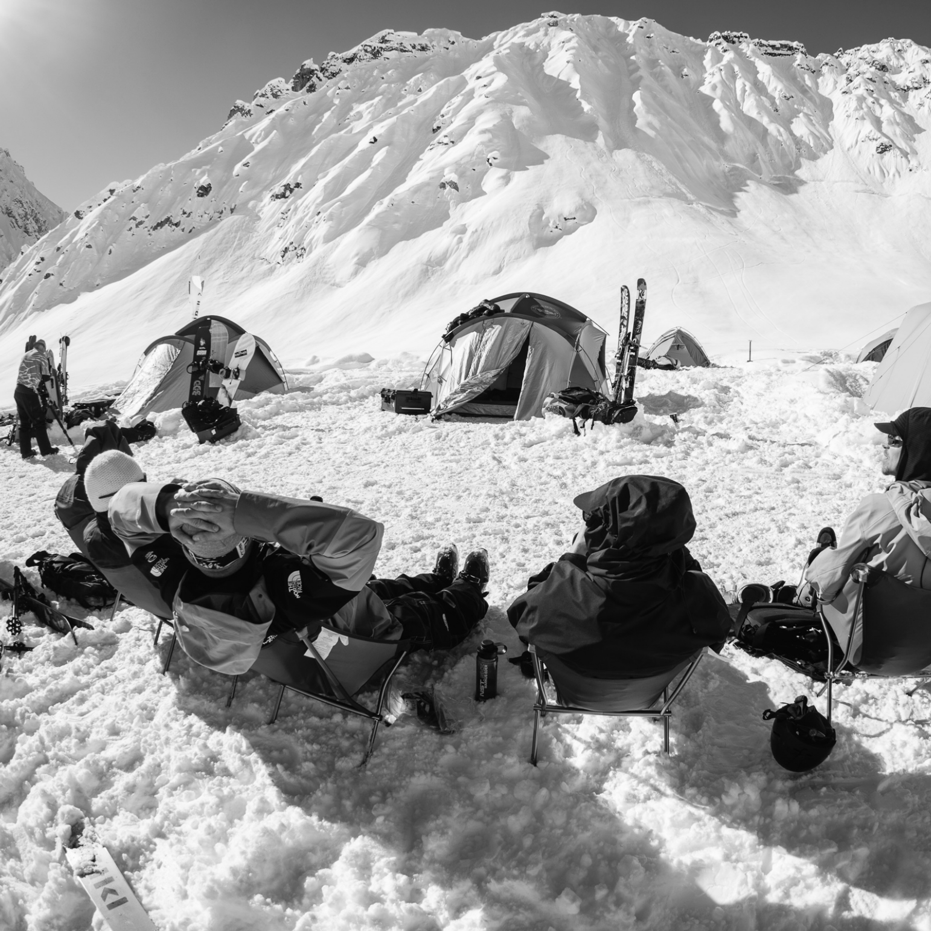 Skiers sitting in a circle with some tents in the background. 