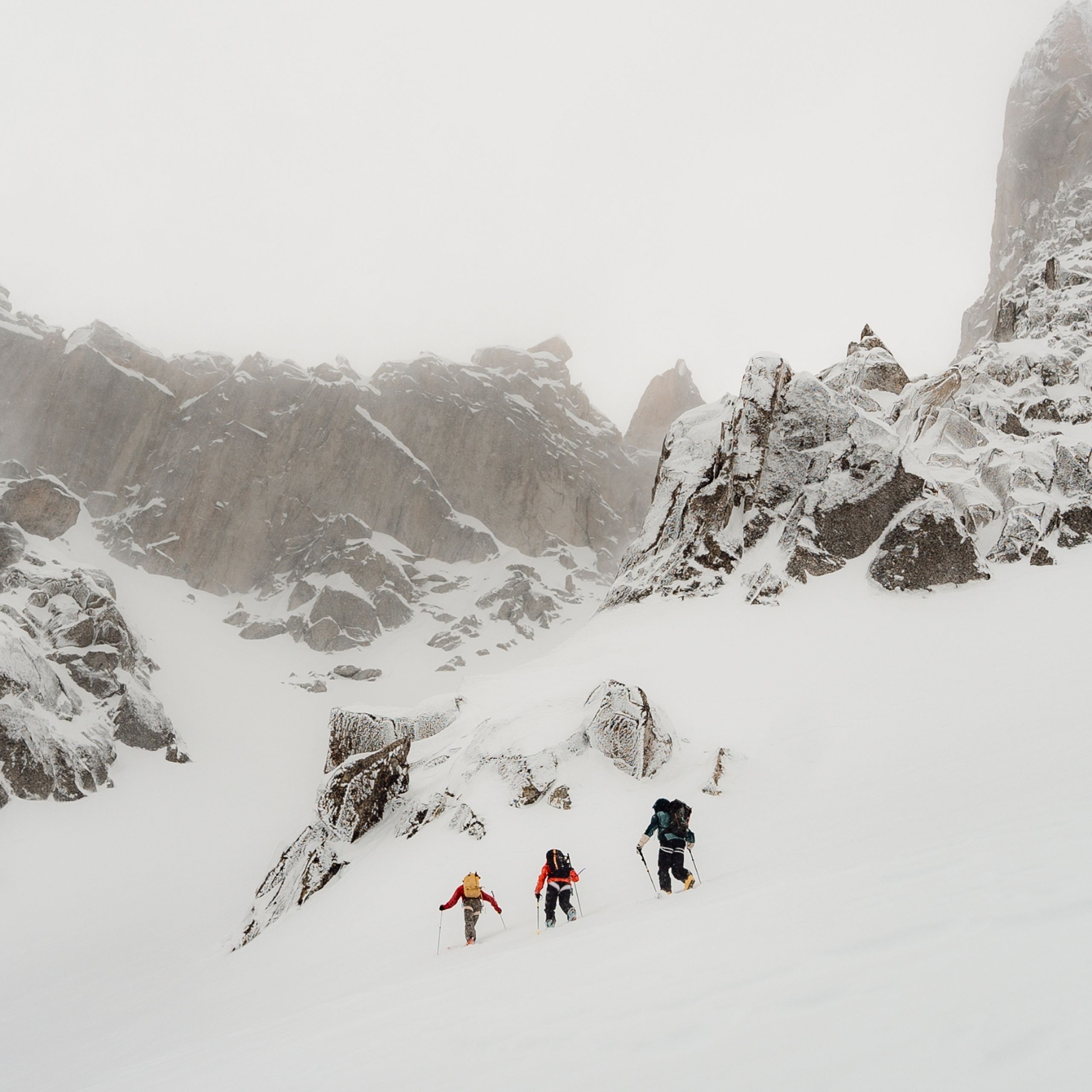 Three skiers ski touring in stormy snow landscape