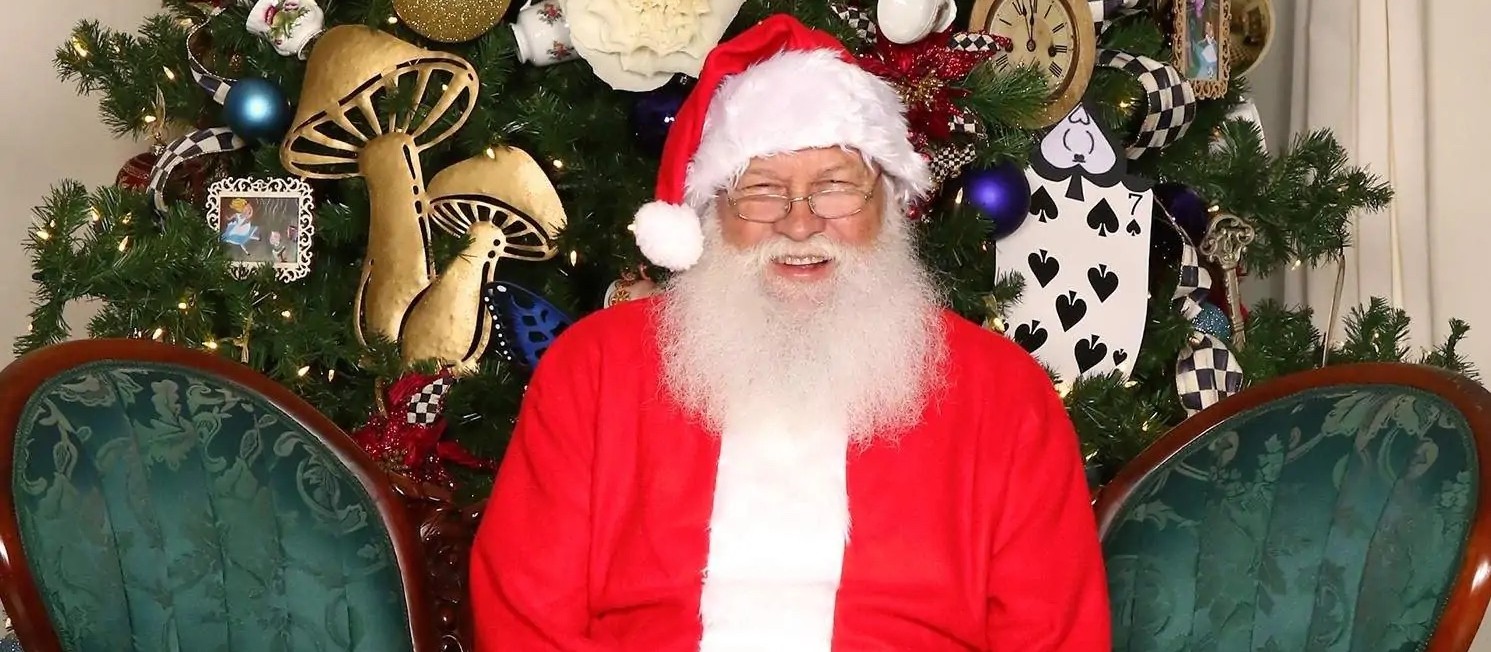 Santa Claus sentado en un sillón verde junto a un árbol de Navidad decorado
