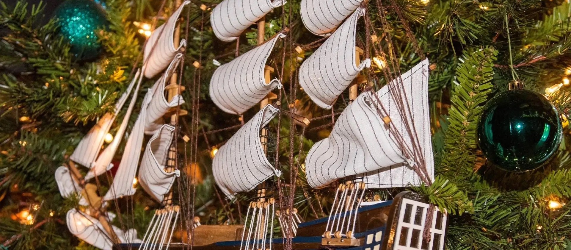 Un adorno en forma de velero colgado entre las luces de un árbol de Navidad