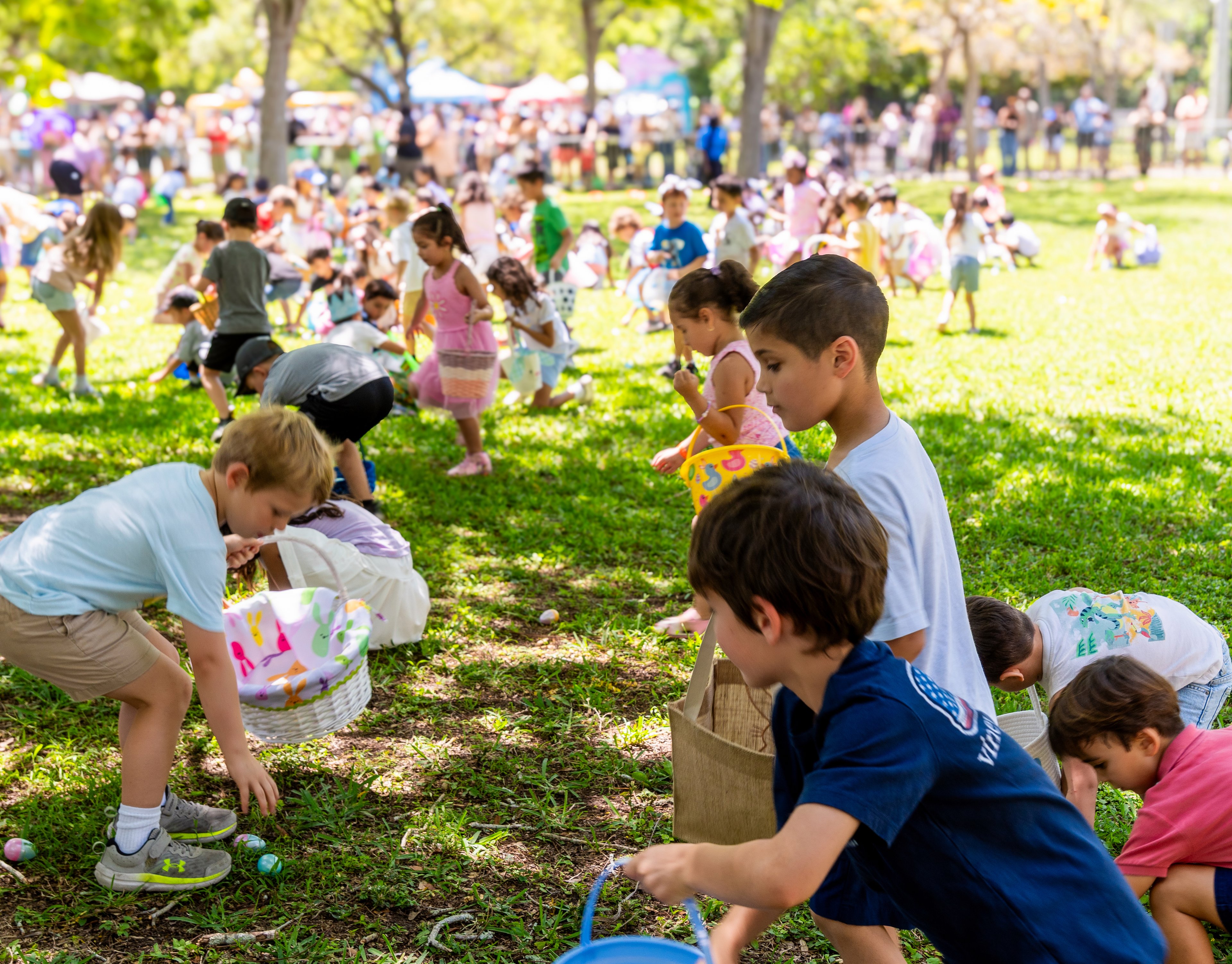 Kids searching for eggs on a park lawn at the Miami Kids Magazine Easter Egg Hunt
