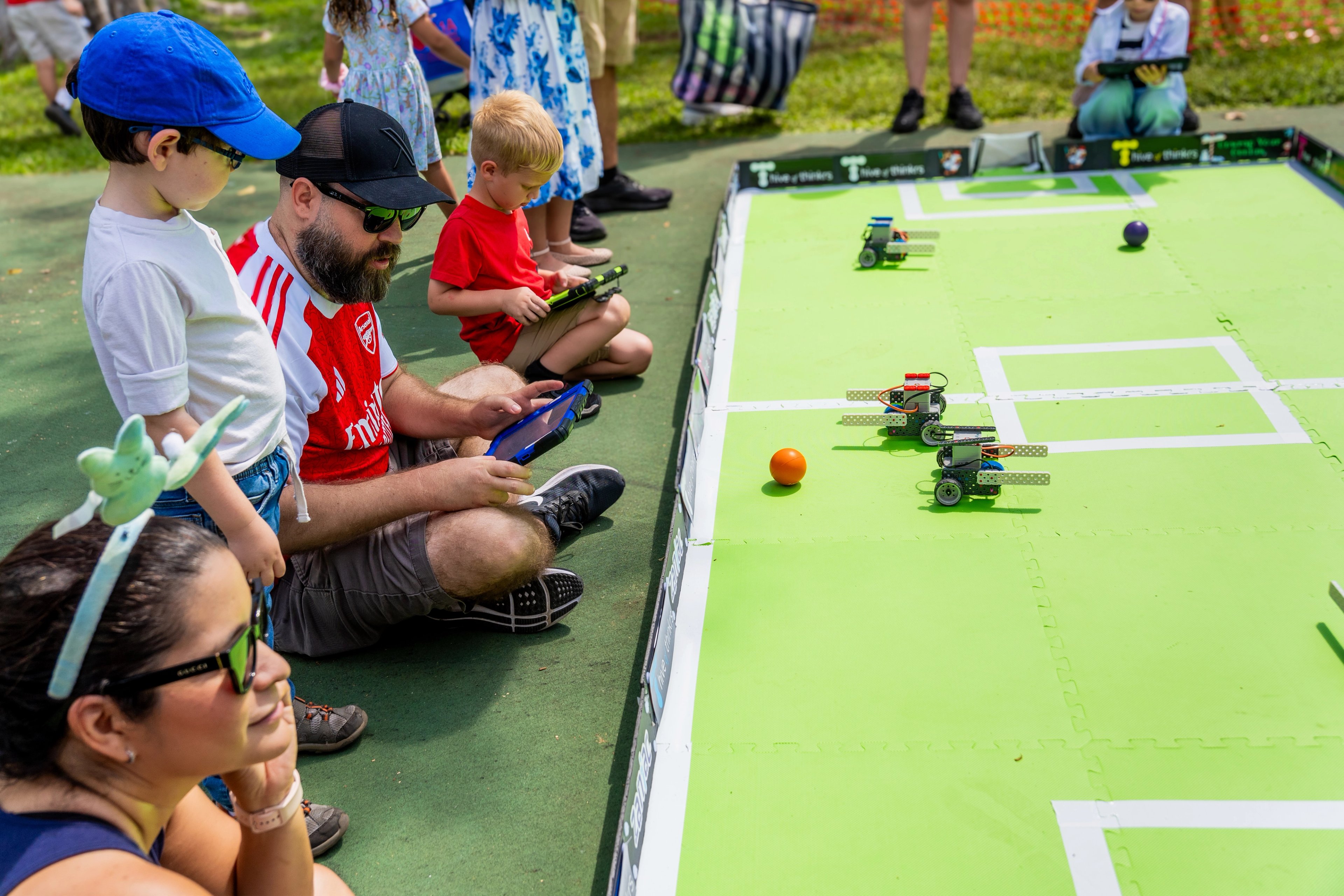 Families watching small robots compete on a Hive of Thinkrs playing field