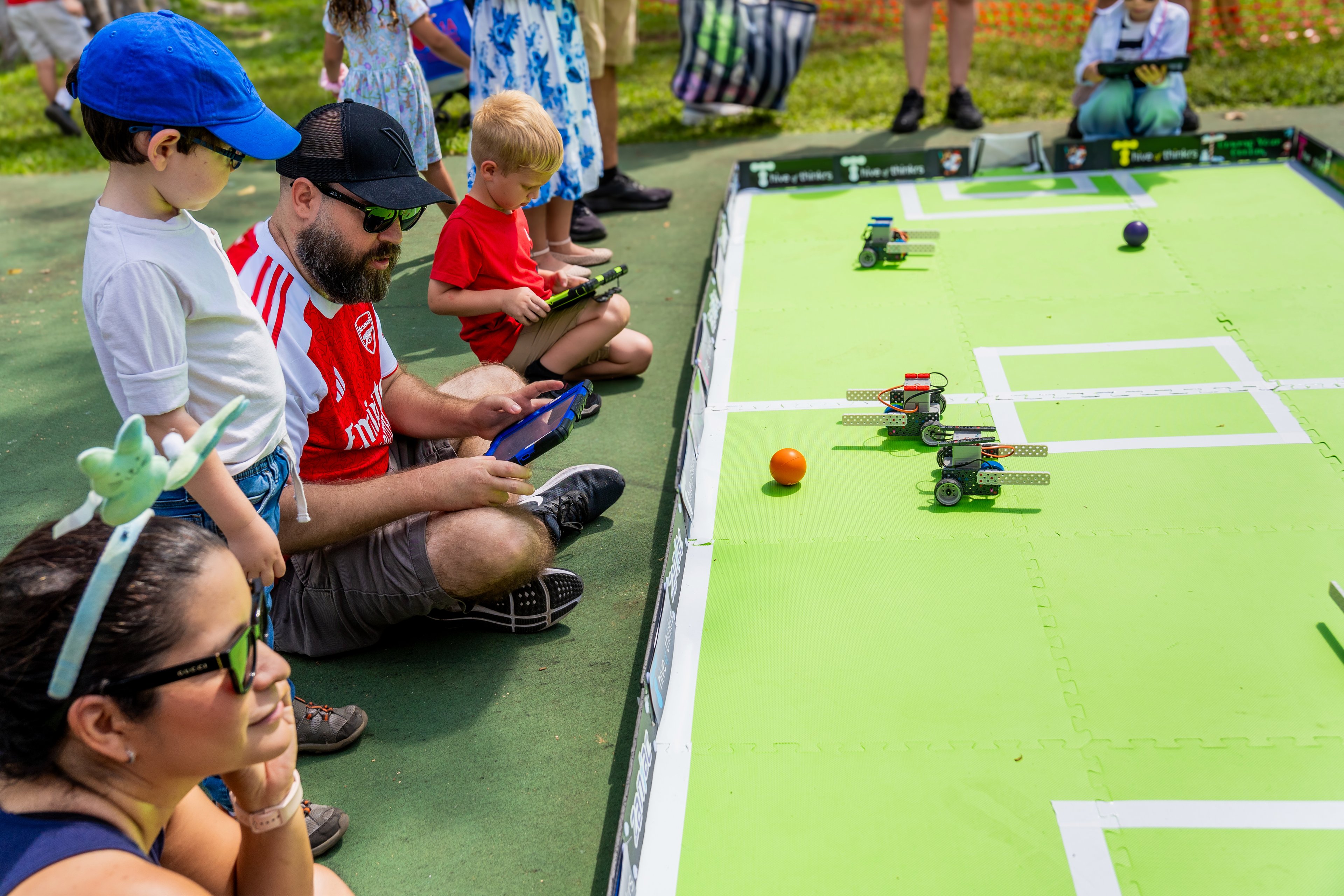 Familias observan pequeños robots compitiendo en una cancha de Hive of Thinkrs