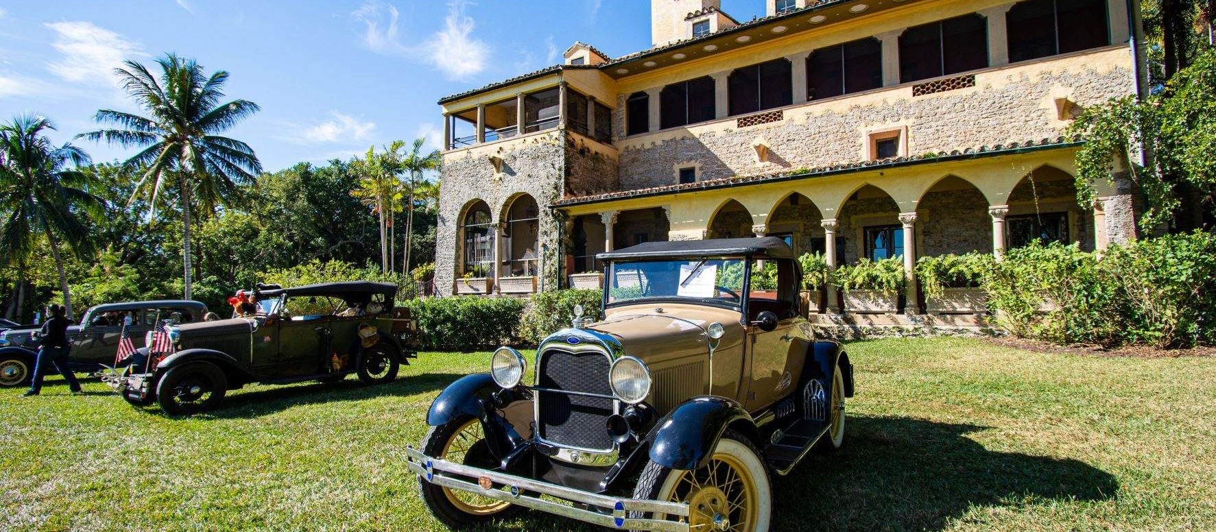Restored vintage cars parked on the lawn in front of the Deering Estate's historic house