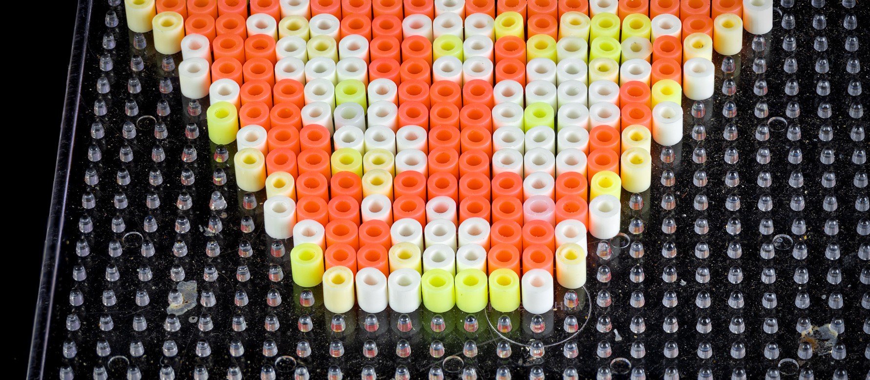 A letter W made of colorful fuse beads on a clear pegboard