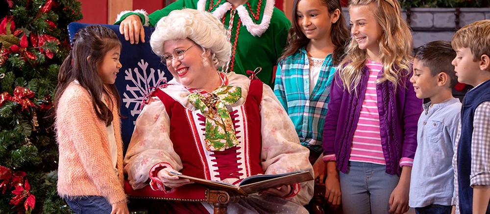 Mrs. Claus leyendo un cuento a un grupo de niños junto a un árbol de Navidad
