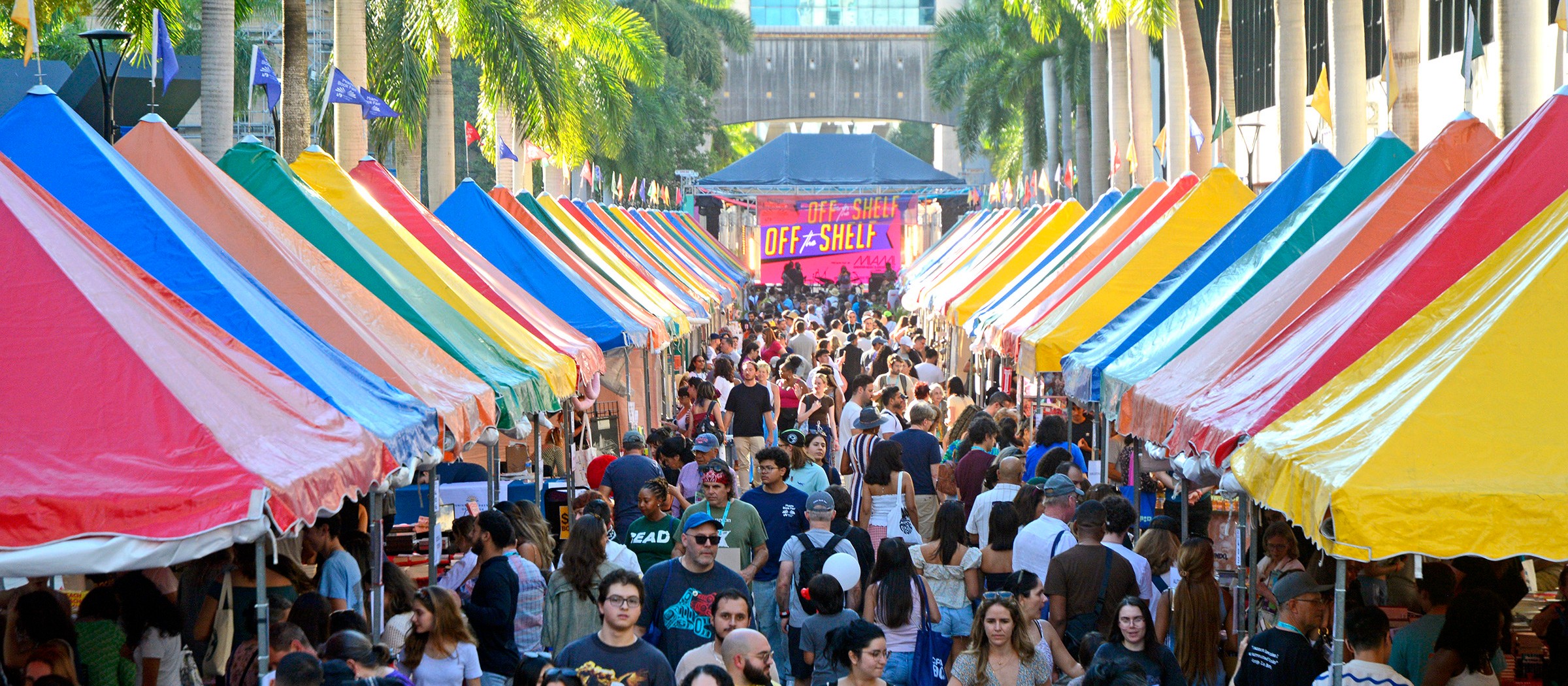 Visitantes caminando entre hileras de carpas de libros de colores en la feria callejera de la Miami Book Fair