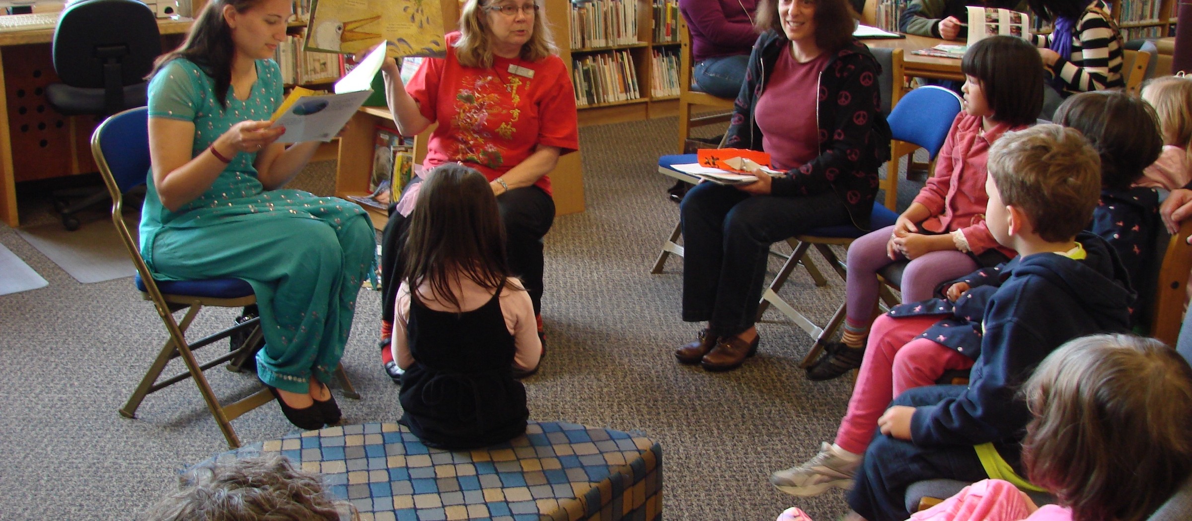 Children sitting on the floor and on chairs, listening to a bilingual storytime in a library