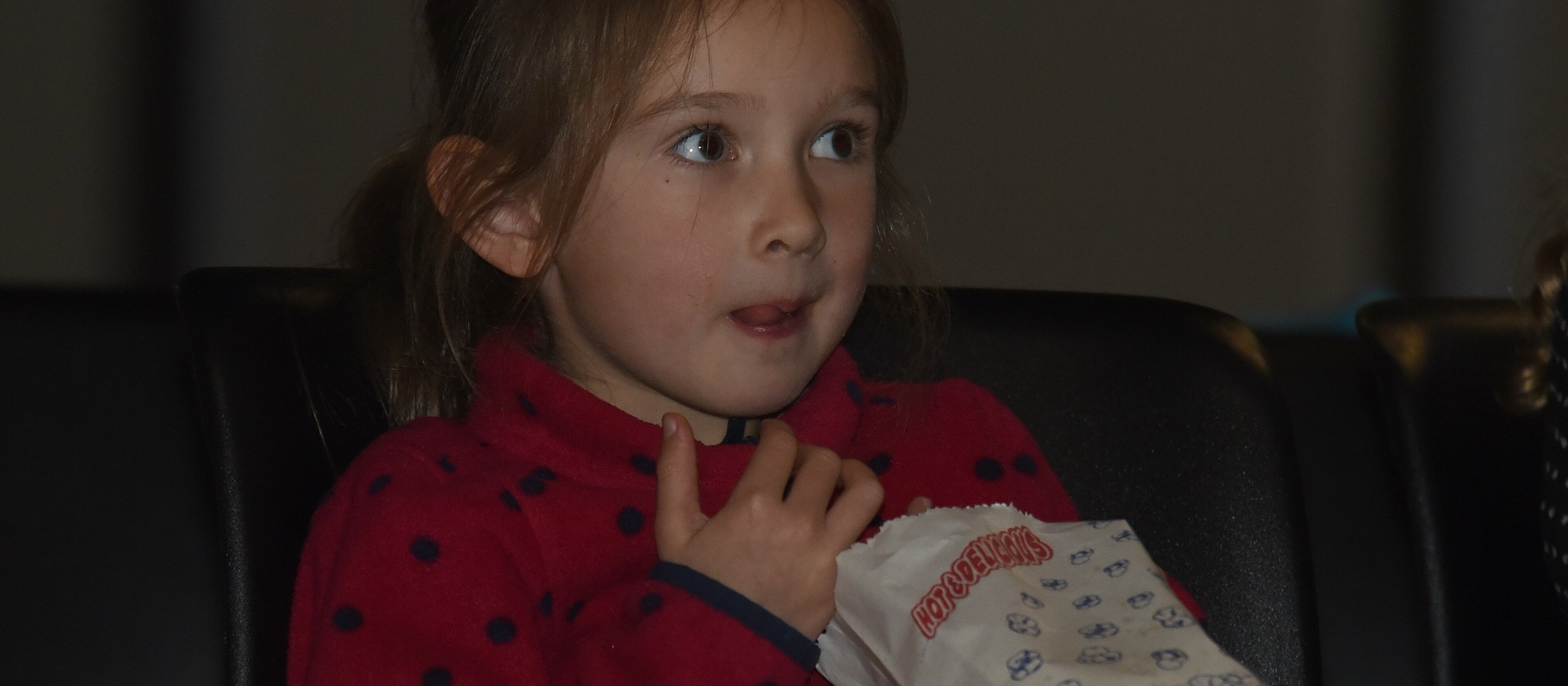 Una niña con una bolsa de palomitas mira una película desde una butaca en una sala oscura
