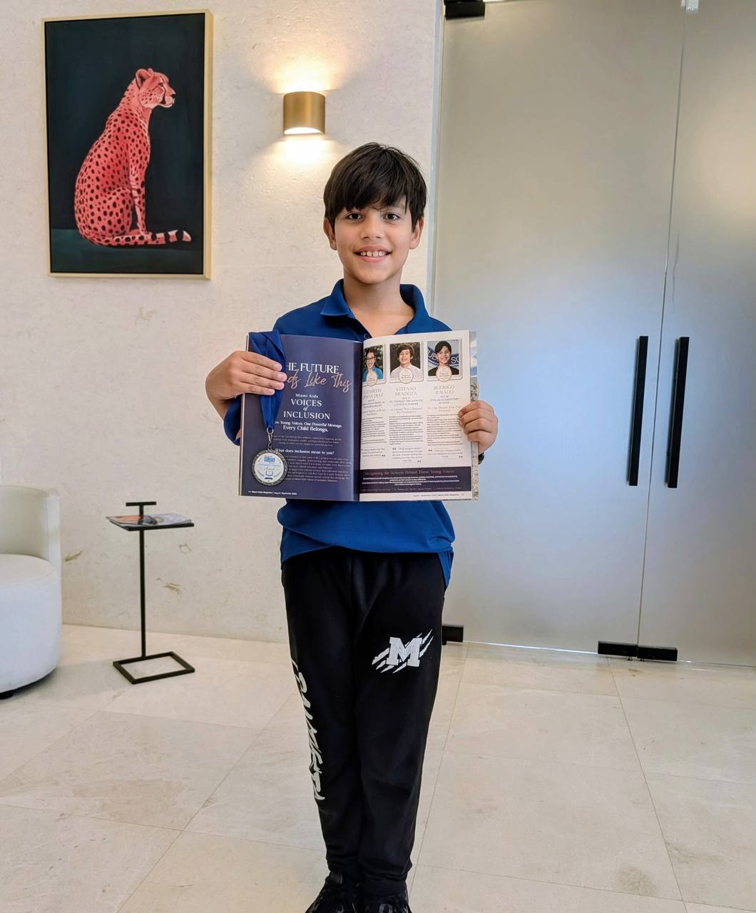 Un niño sostiene abiertas las páginas de Voices of Inclusion de la revista, con su medalla colgando de ellas