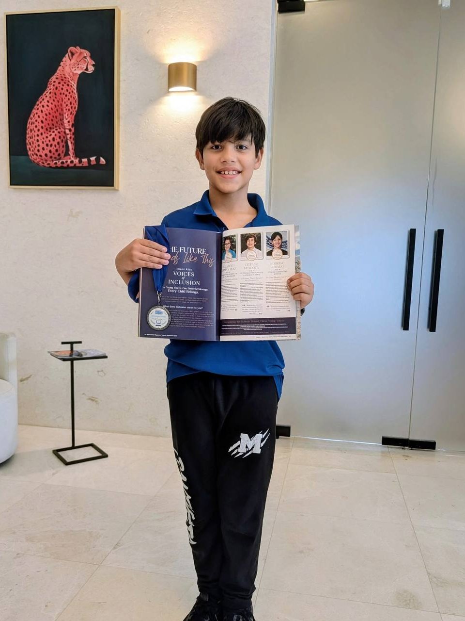 Un niño sostiene abiertas las páginas de Voices of Inclusion de la revista, con su medalla colgando de ellas