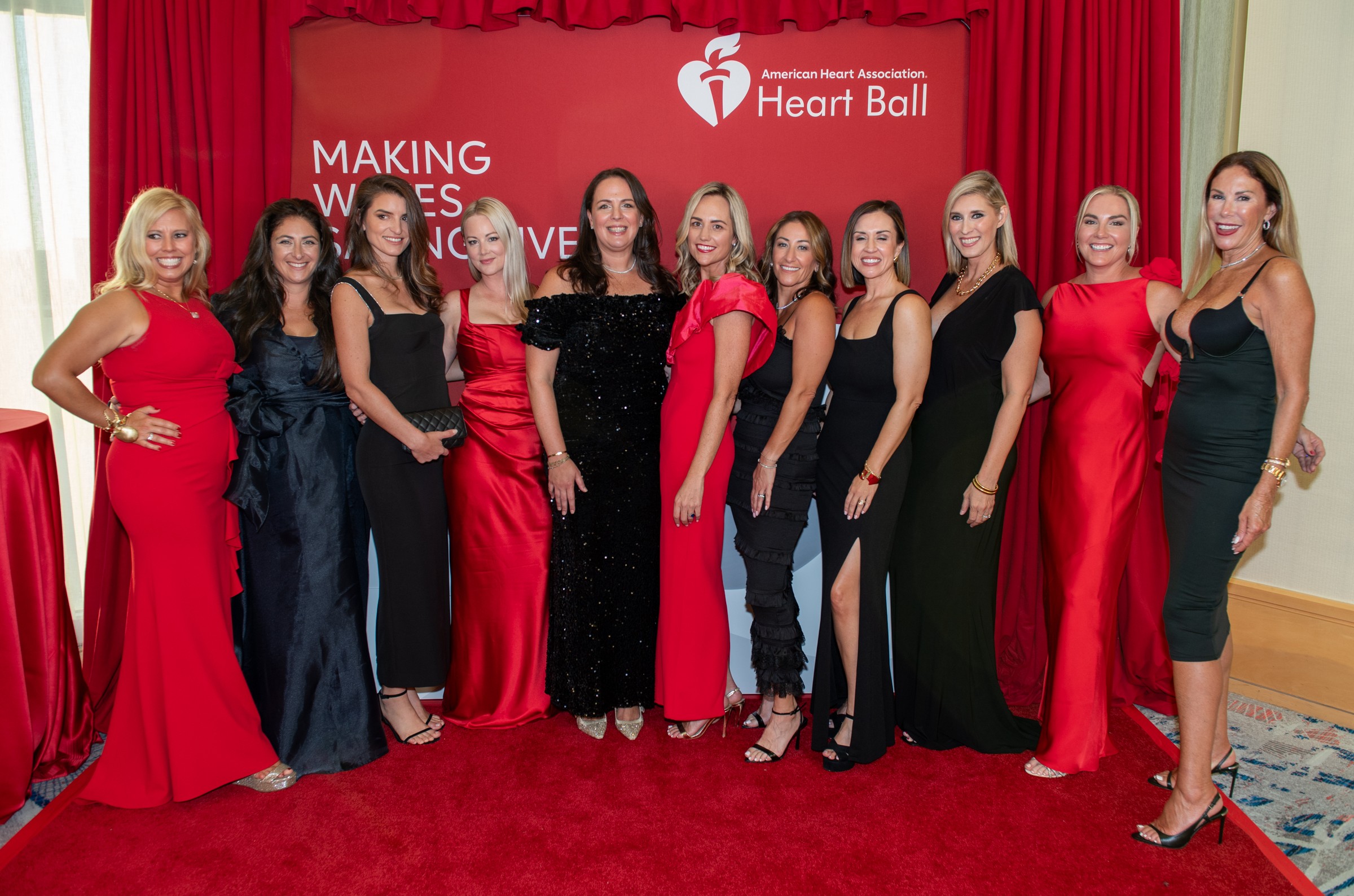 Invitadas con vestidos rojos y negros ante el panel del Heart Ball