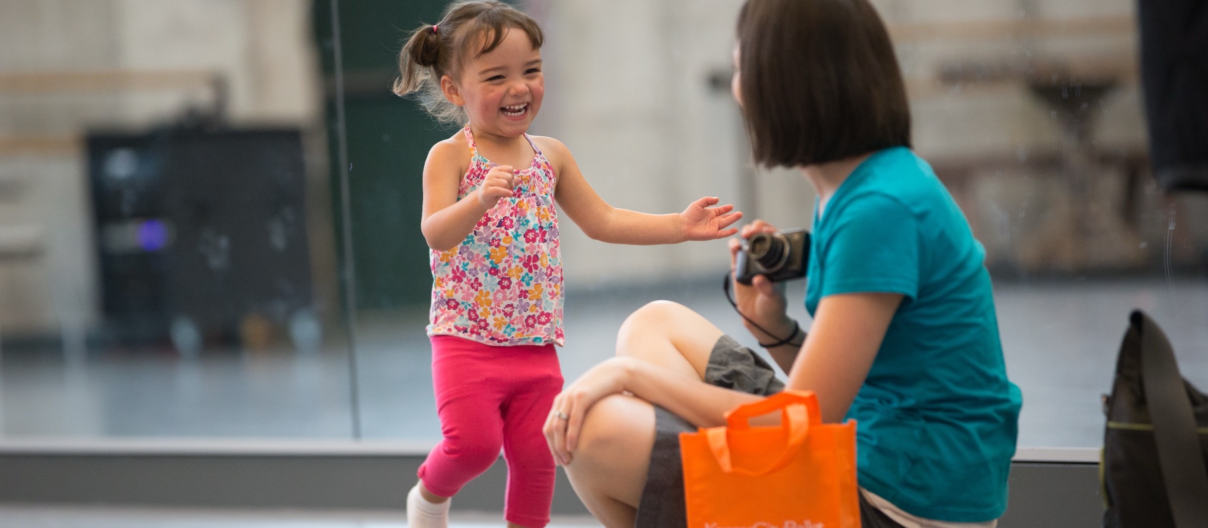 Una niña pequeña sonriente baila frente a una maestra durante una clase de movimiento