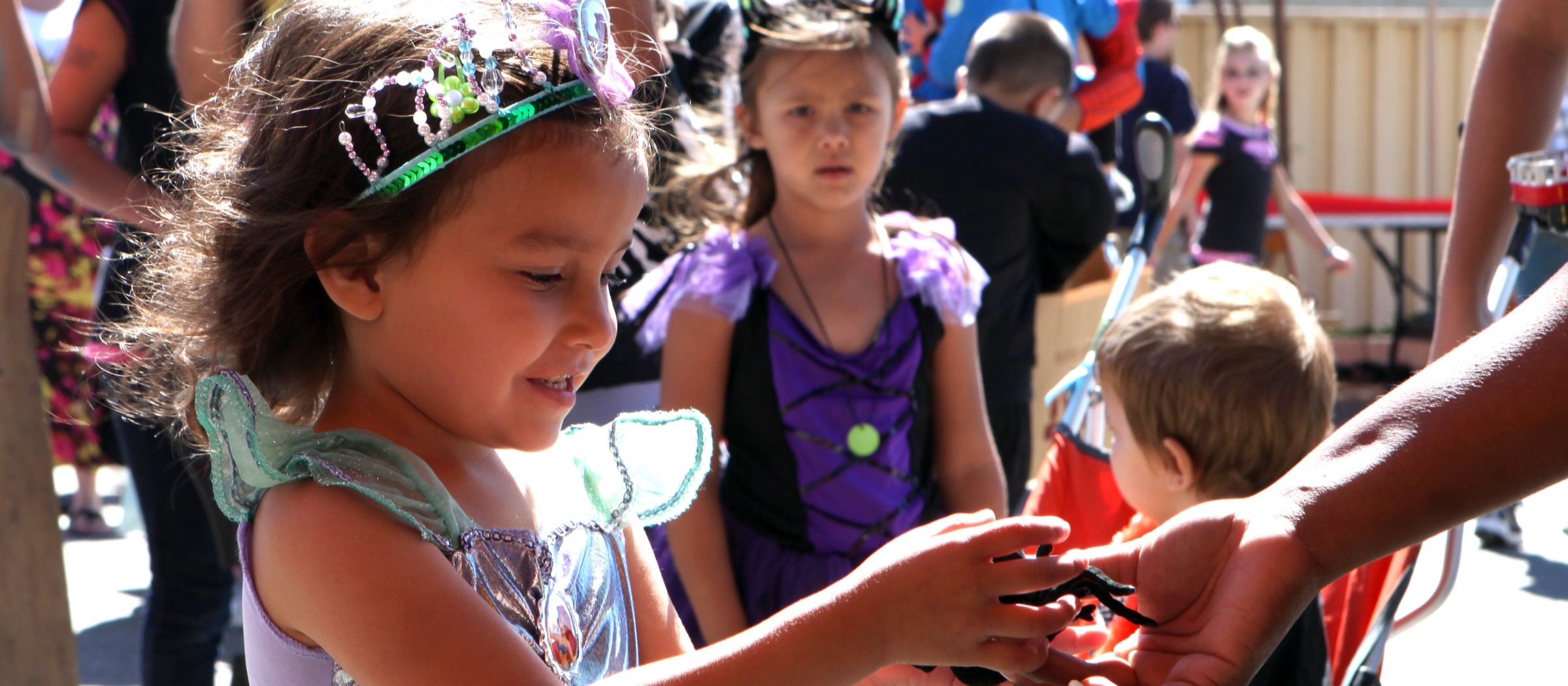 Una niña con disfraz de hada y tiara recibe un premio en un carnaval de Halloween, con otros niños disfrazados esperando detrás