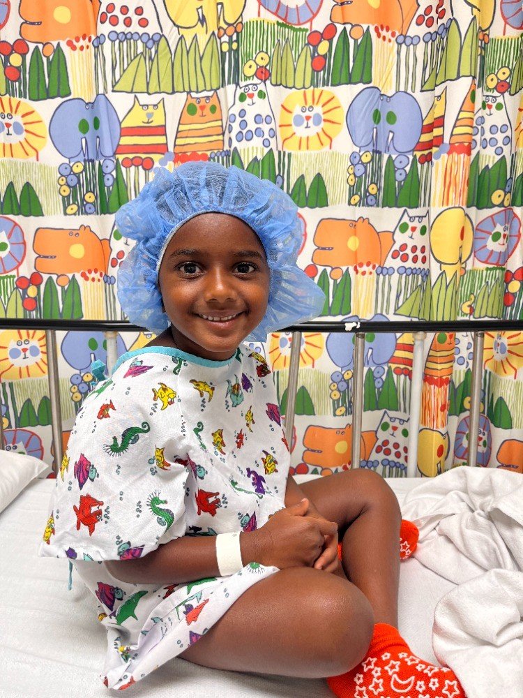 Jamie sonríe en una cama de hospital, con bata y gorro quirúrgico