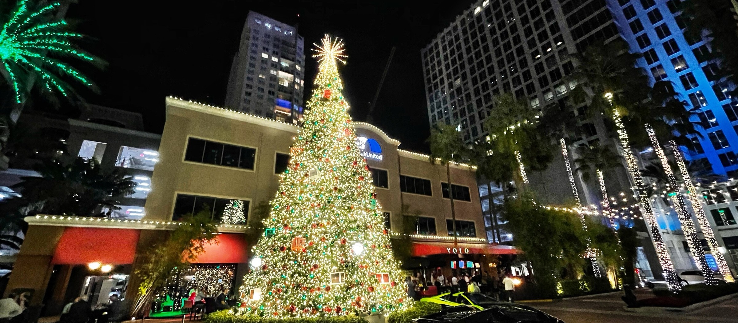 A tall lit Christmas tree on a plaza in downtown Fort Lauderdale at night